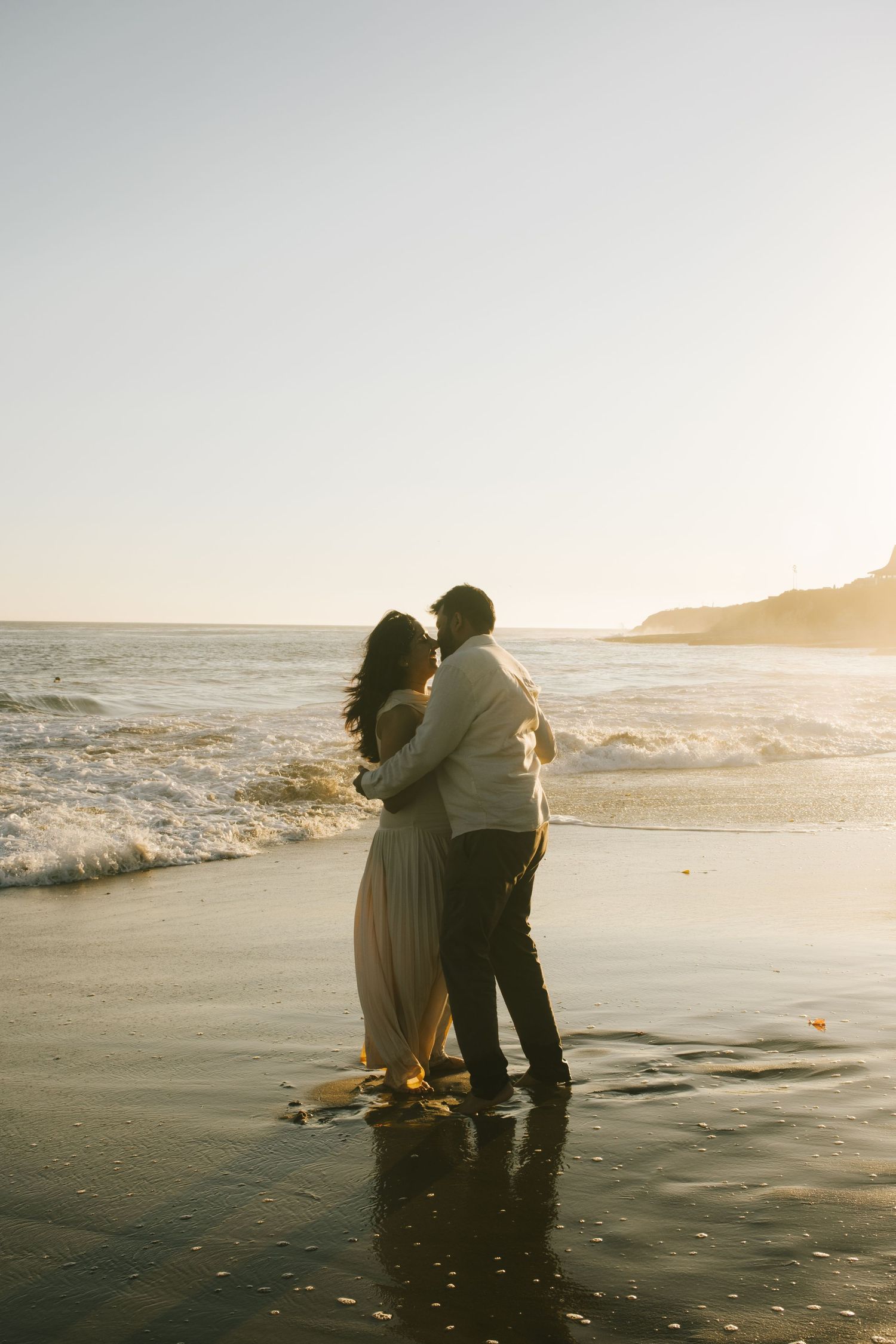 A couple shares a tender moment on the beach at golden hour.