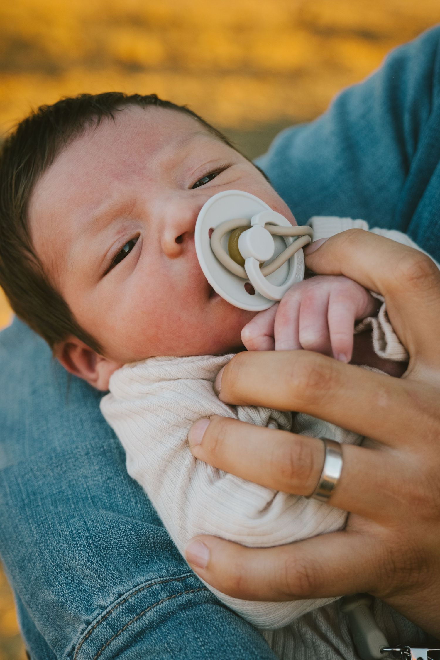 Baby with pacifier resting peacefully against blue denim in golden light.