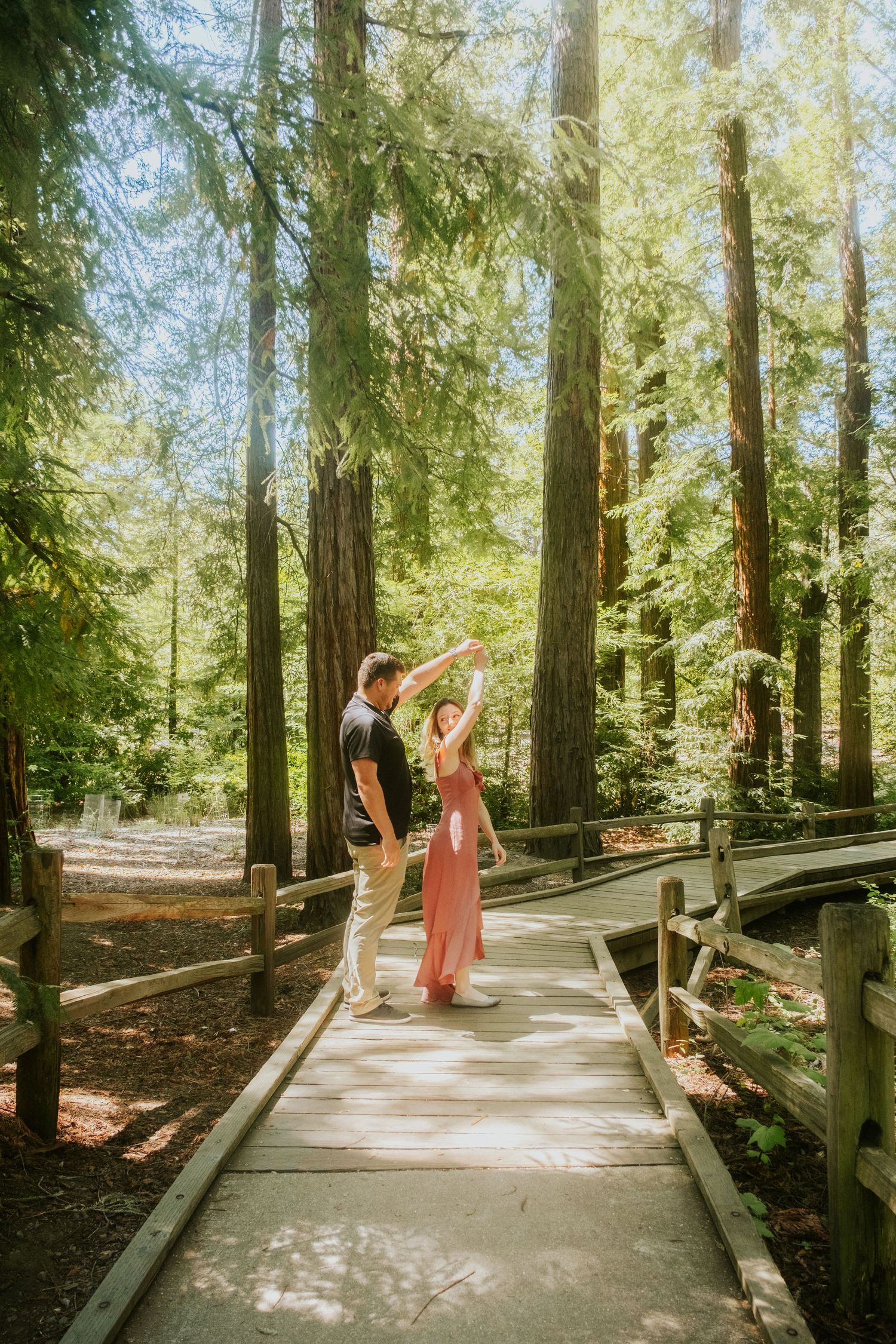 Couple dancing on wooden boardwalk surrounded by tall redwood trees.