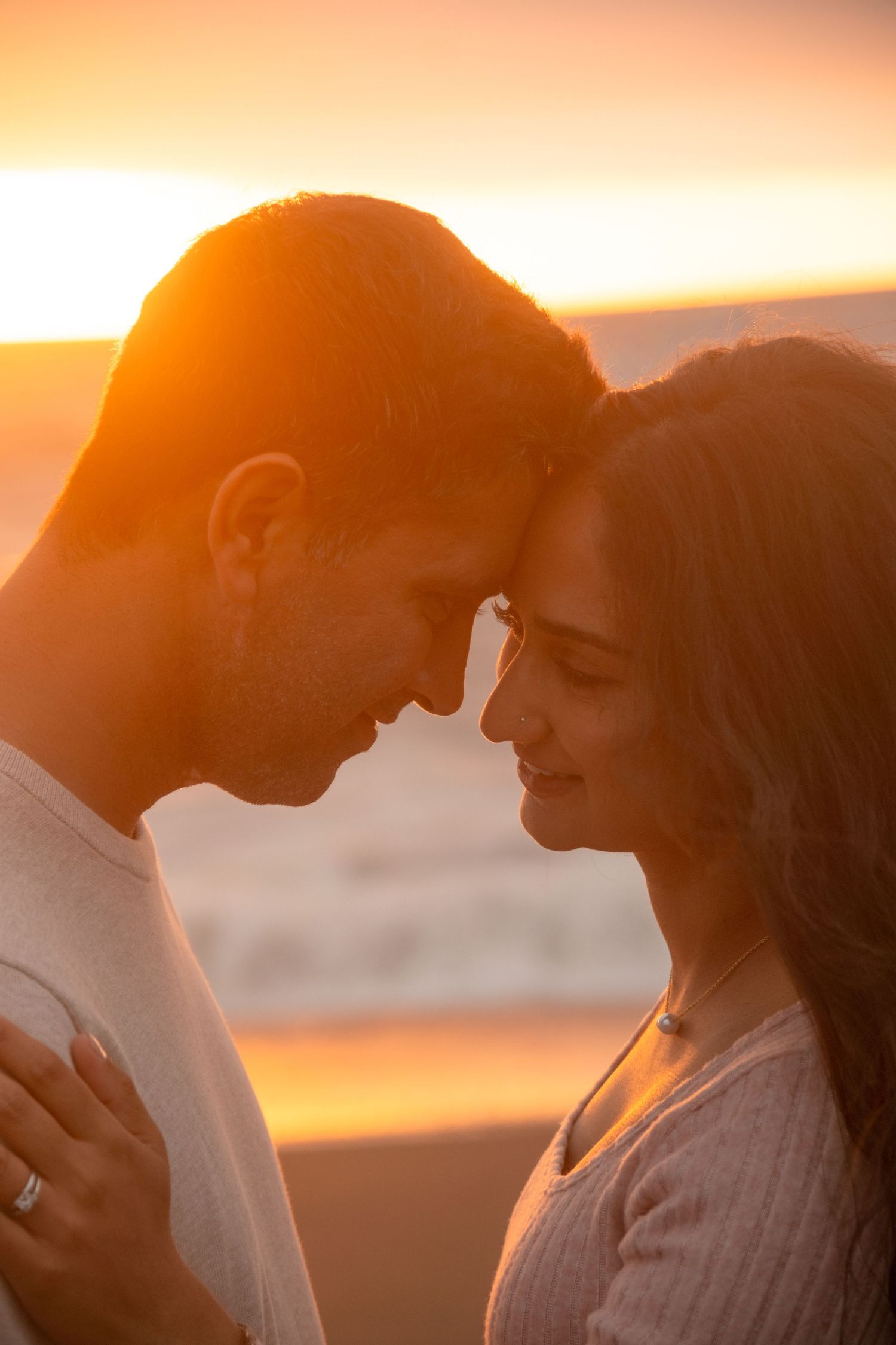 Romantic couple silhouetted against warm sunset sky share intimate moments at the beach.