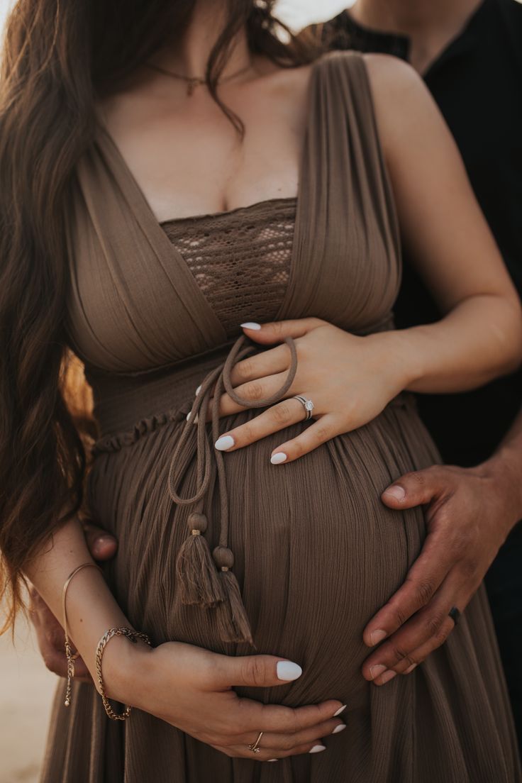 Close-up of hands cradling pregnant belly in brown maternity dress.