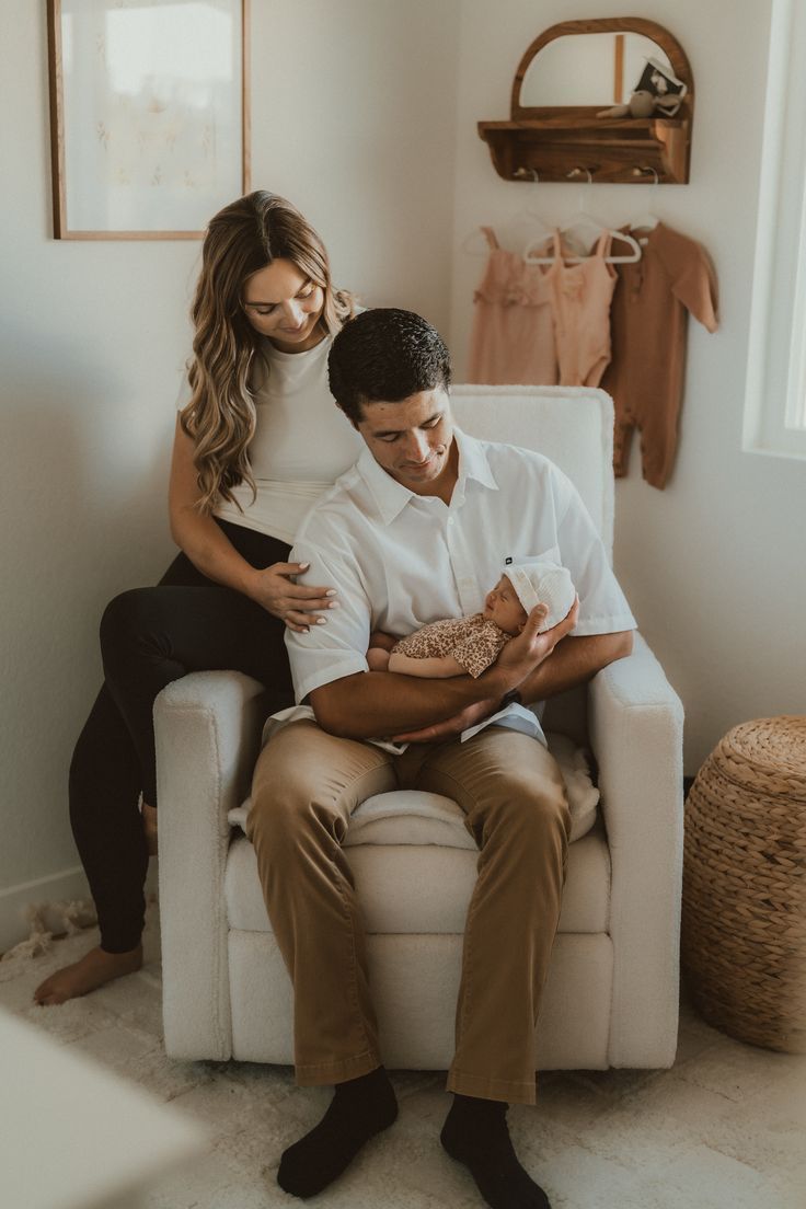 A couple sits together on a white armchair in a minimalist room with natural decor elements.