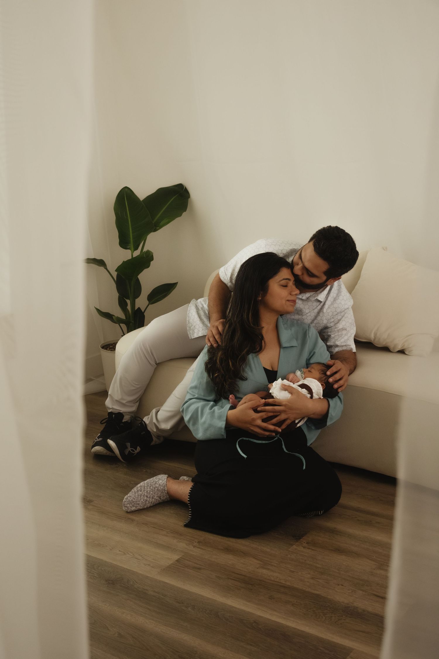 Family bonding with newborn on hardwood floor near indoor plants.