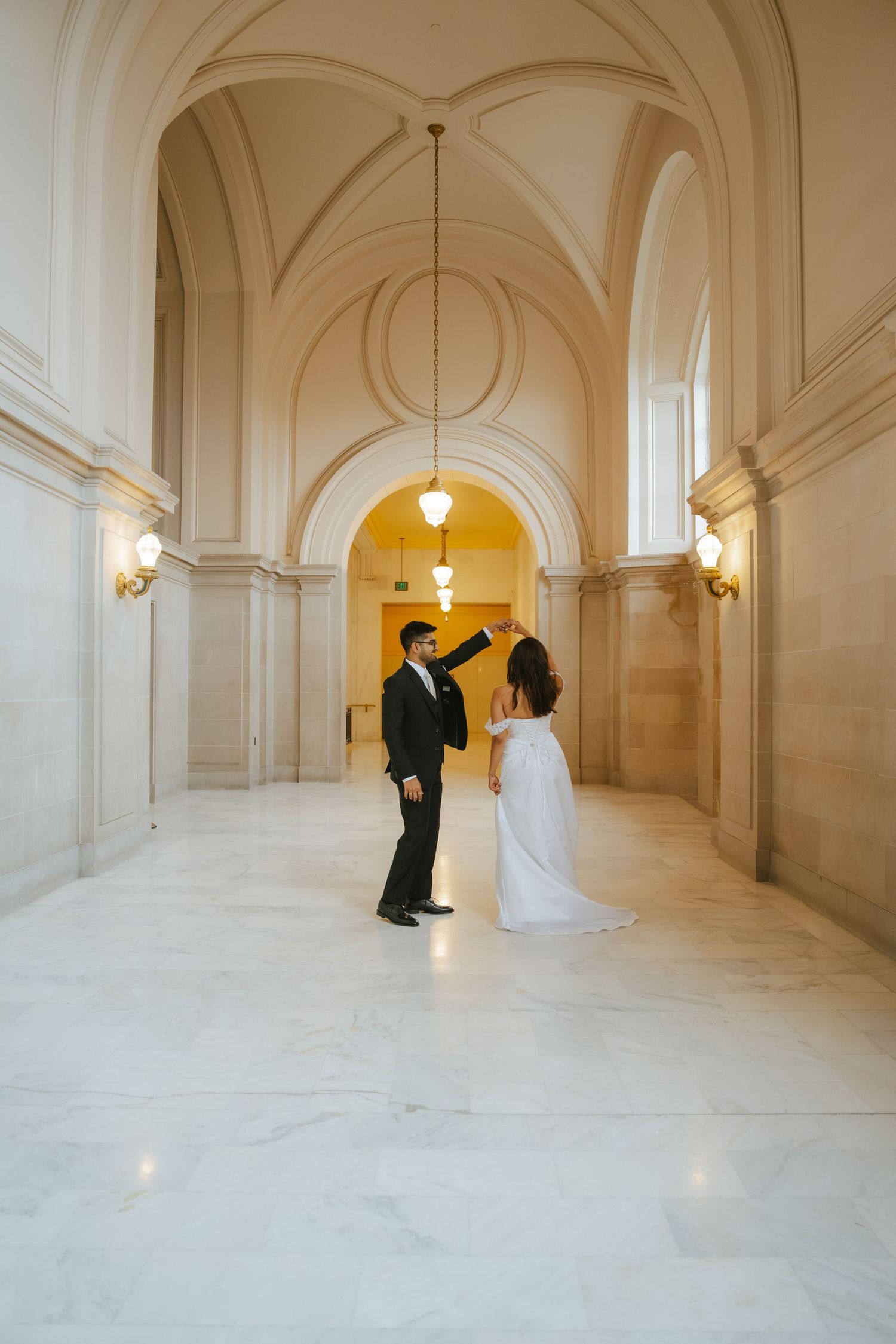 Bride and groom dancing in elegant marble hallway with arched ceilings at San Francisco City Hall wedding.