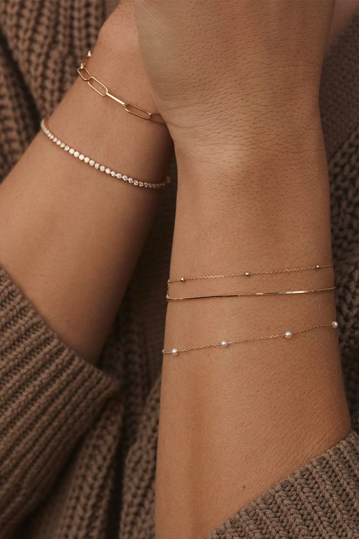 Delicate gold chain bracelets layered on wrist against brown knit fabric.