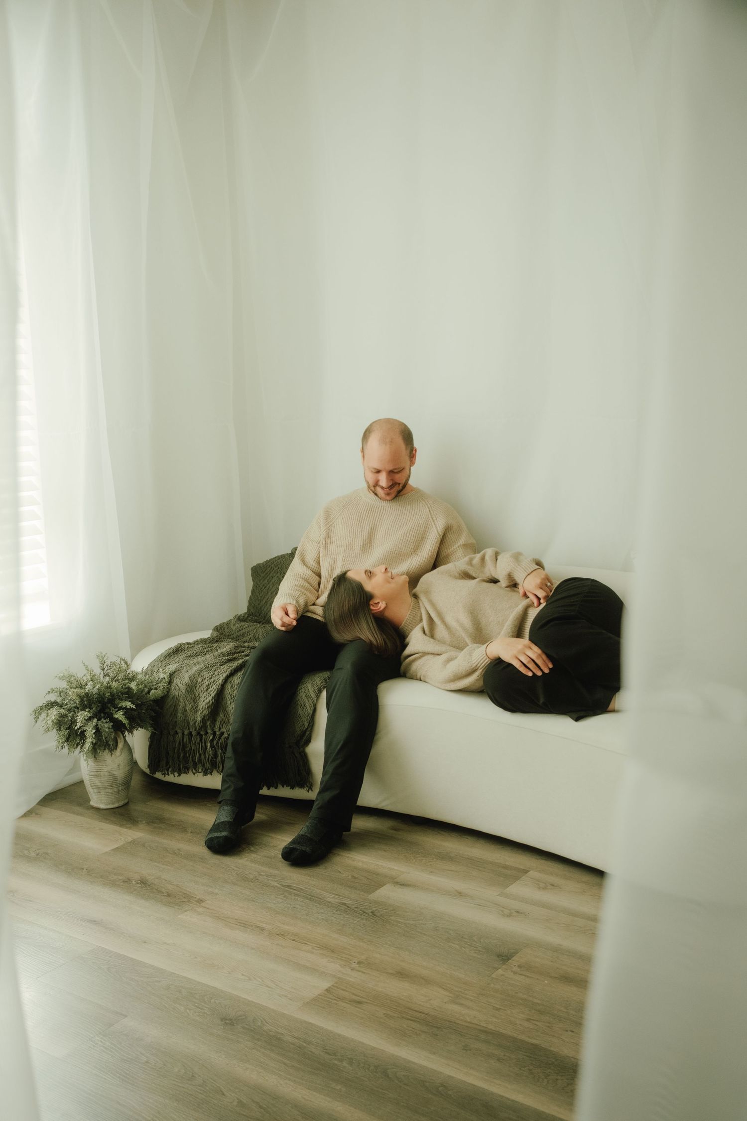 A couple relaxing together on a white couch with a cozy blanket and indoor plant.