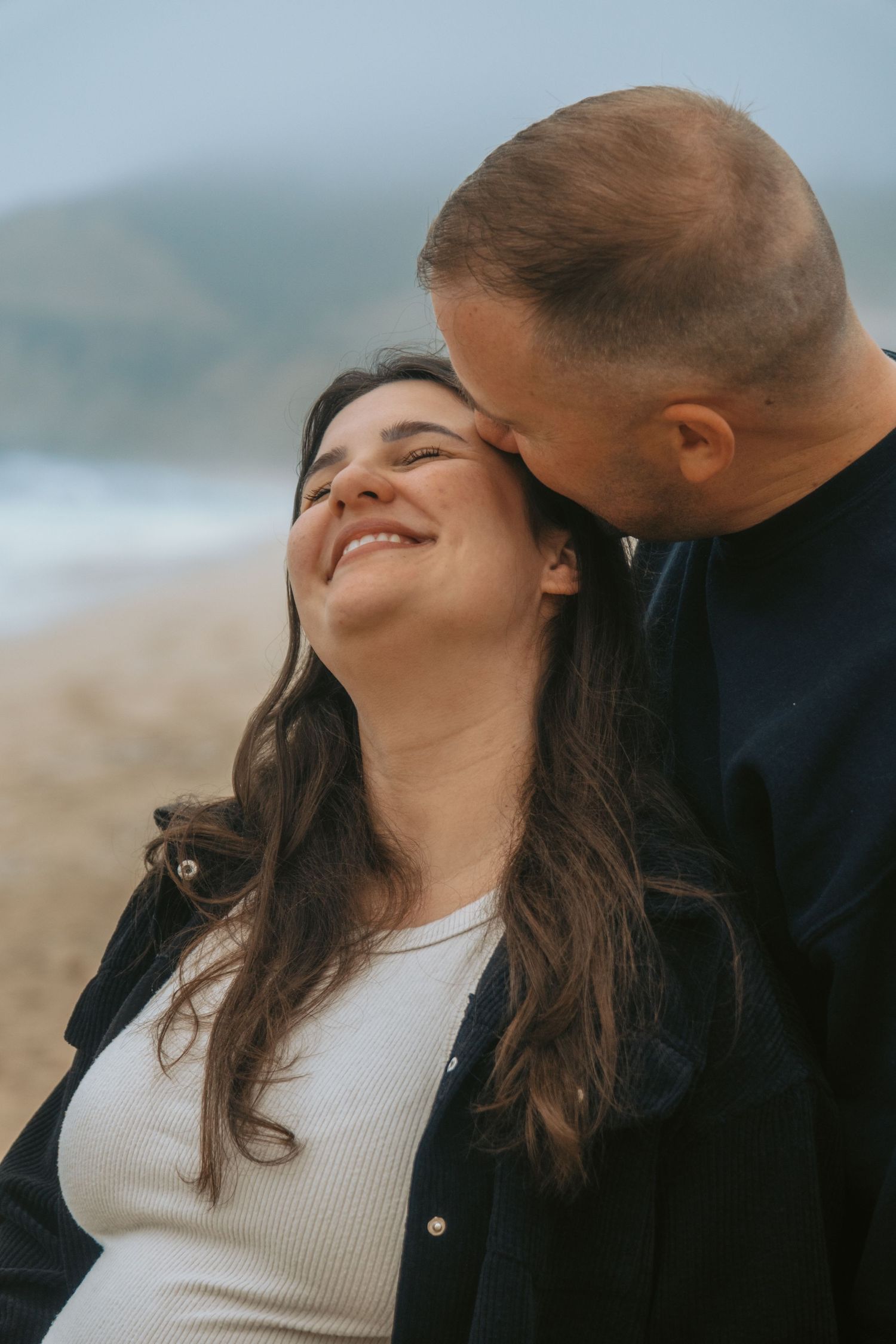 Joyful maternity photos captured against coastal backdrop during golden hour.
