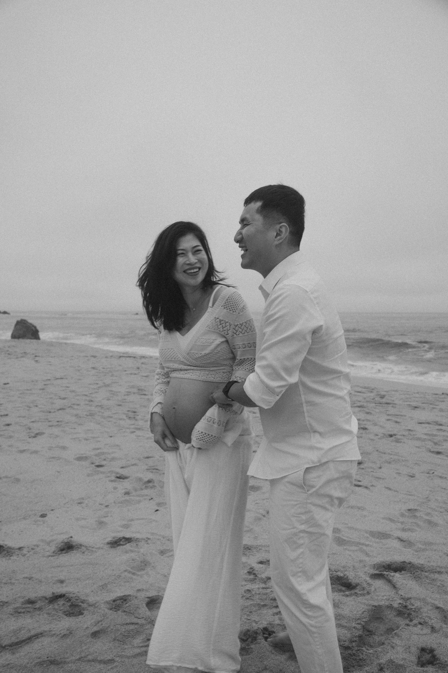 A couple embraces lovingly on a misty beach in black and white photography.