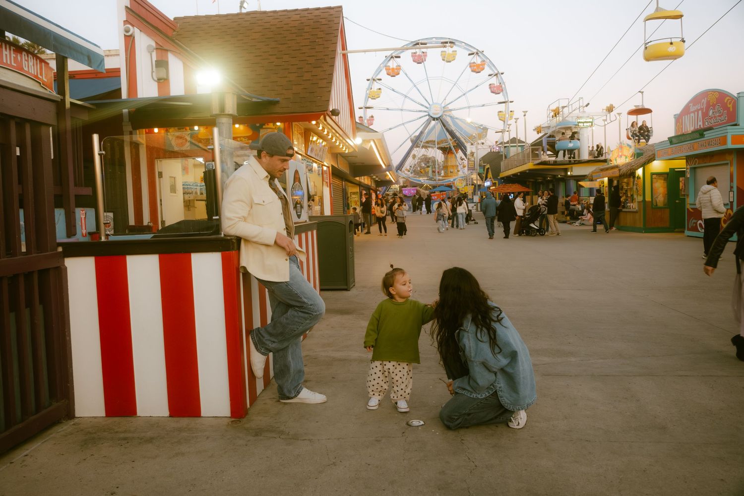 Family enjoying a colorful amusement park boardwalk at dusk with a Ferris wheel in the background.