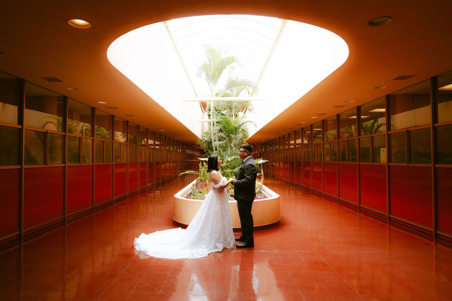 Bride and groom share a romantic moment in a stunning modern corridor with red walls and skylight.