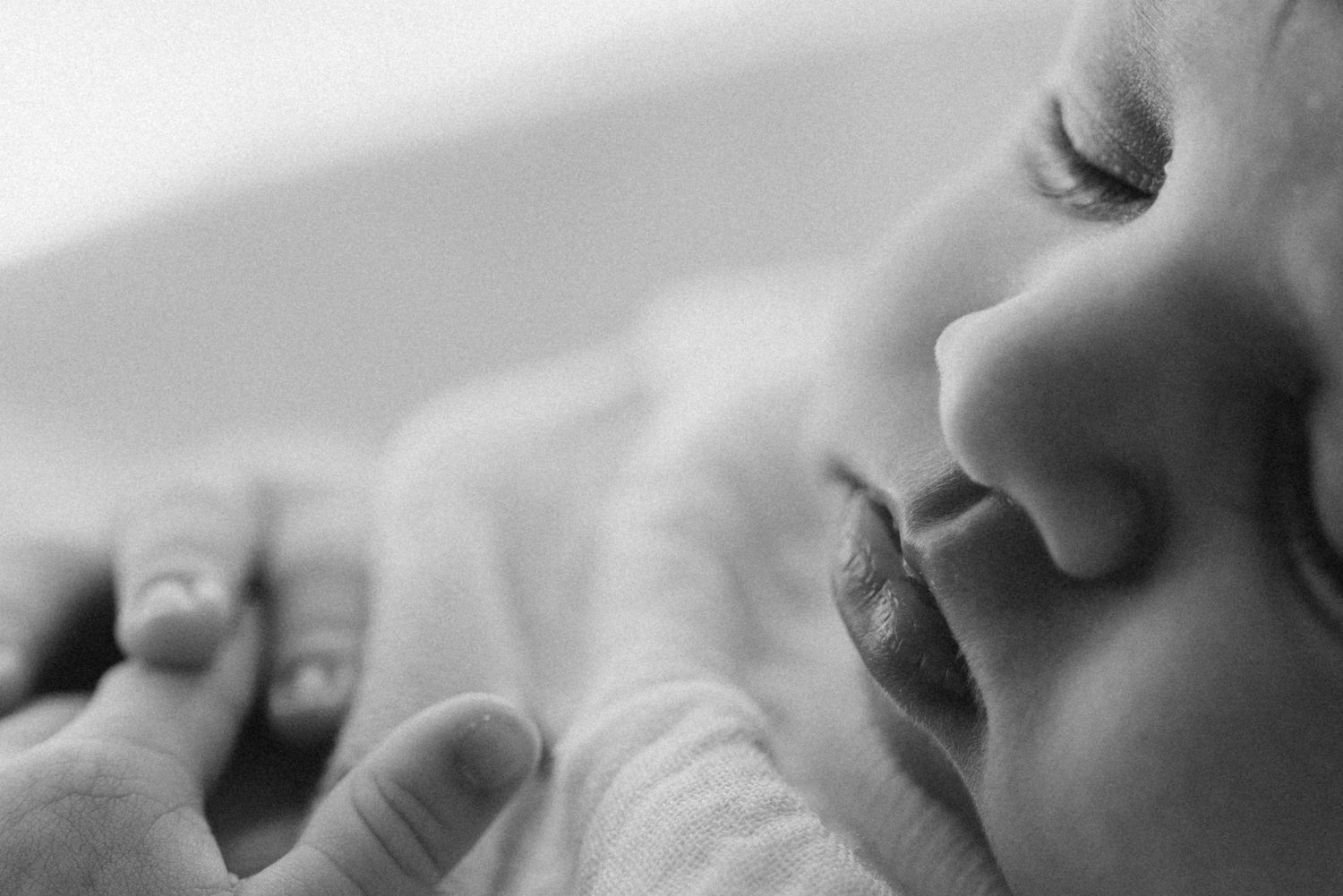 Close-up black and white photo of a sleeping newborn baby with delicate features and tiny fingers.