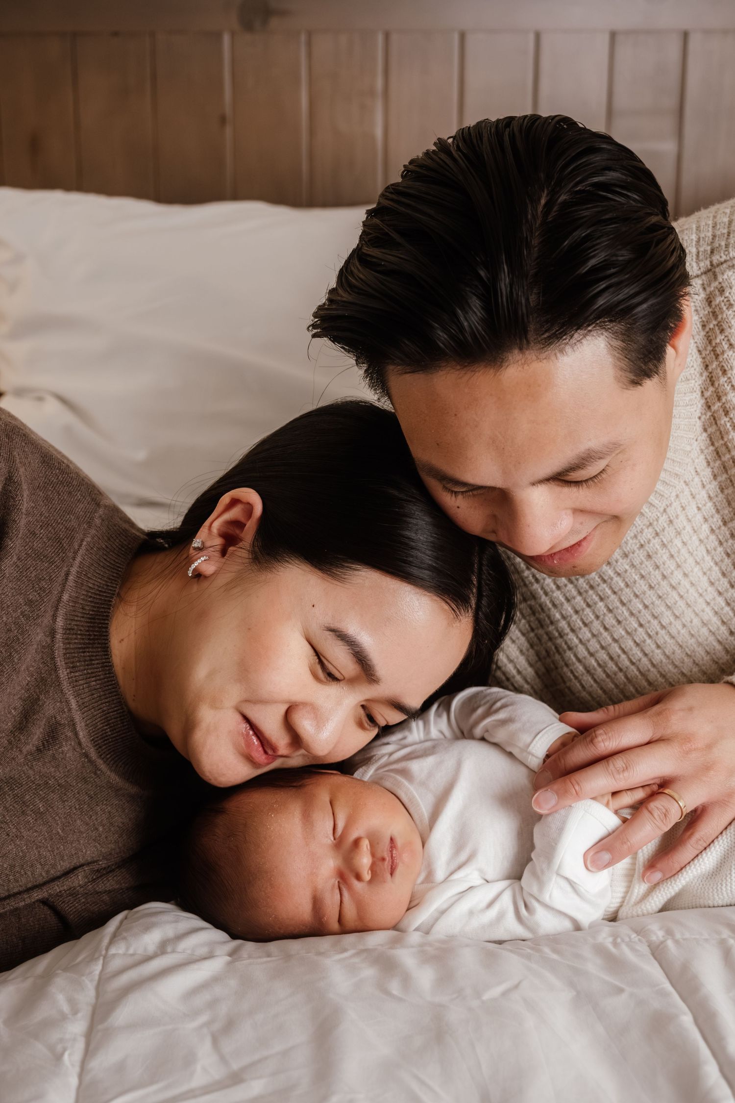 A tender moment as parents cuddle with their sleeping newborn baby on white bedding.