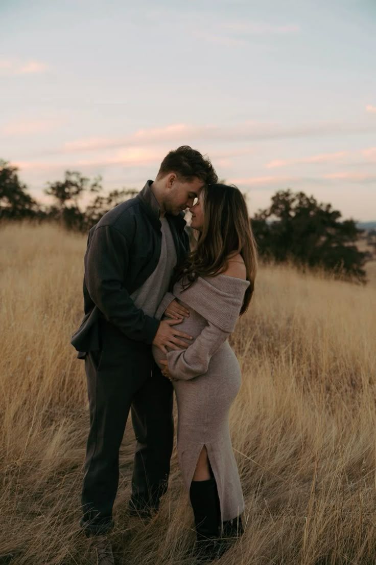 Couple shares intimate moment in golden grass field during sunset.