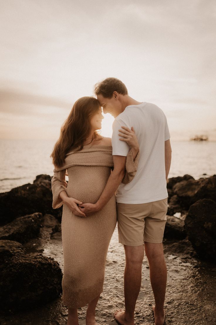Couple embracing on rocky beach during golden hour.