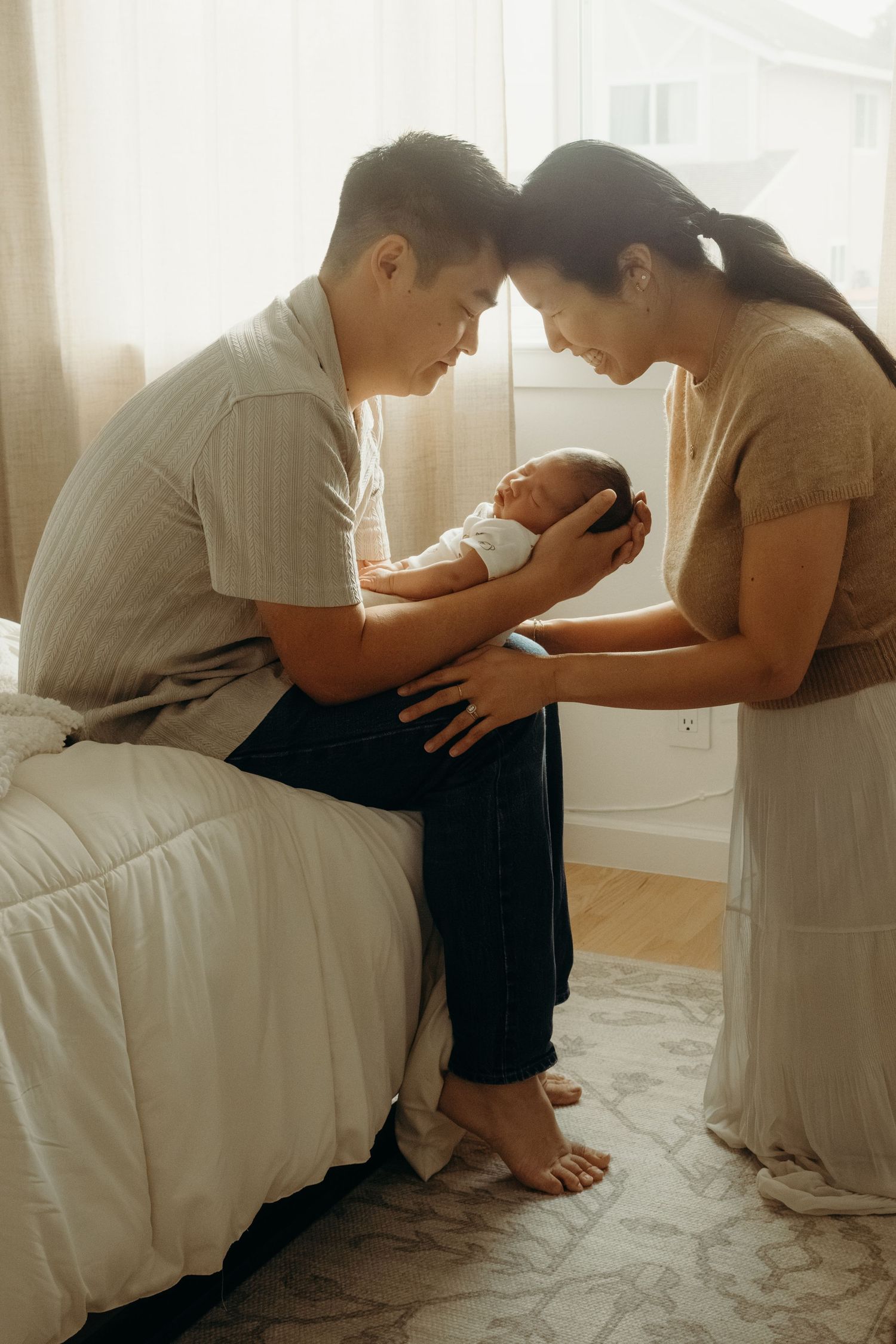 Parents gazing lovingly at their newborn baby while sitting on a bed.