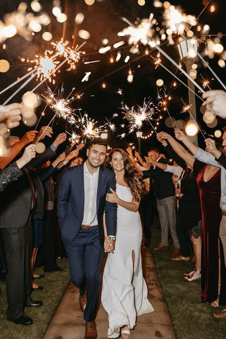 Newlyweds walk through a sparkler send-off tunnel at nighttime wedding celebration with guests lining the path.