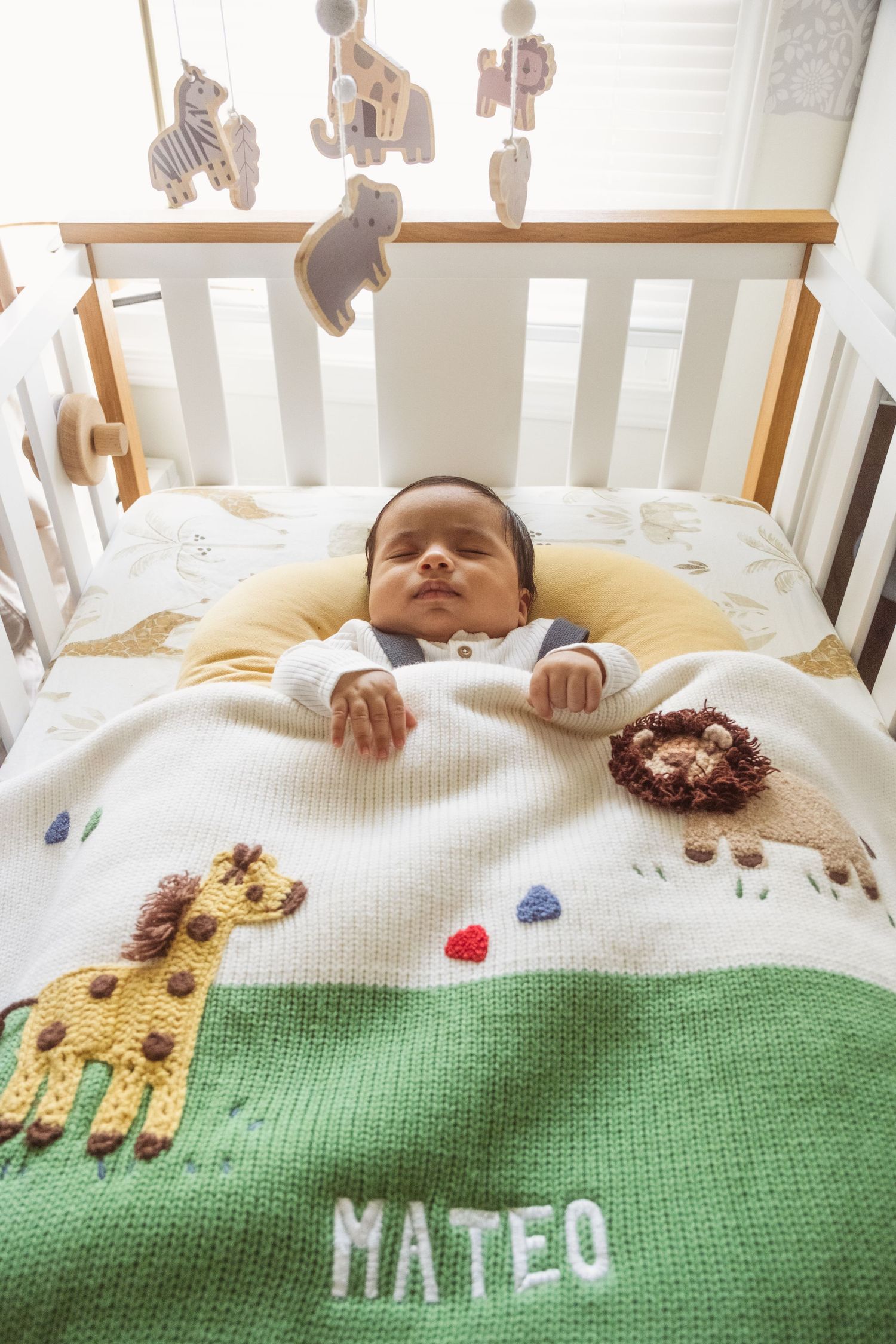 Baby crib with white and green knitted blanket featuring animal designs.