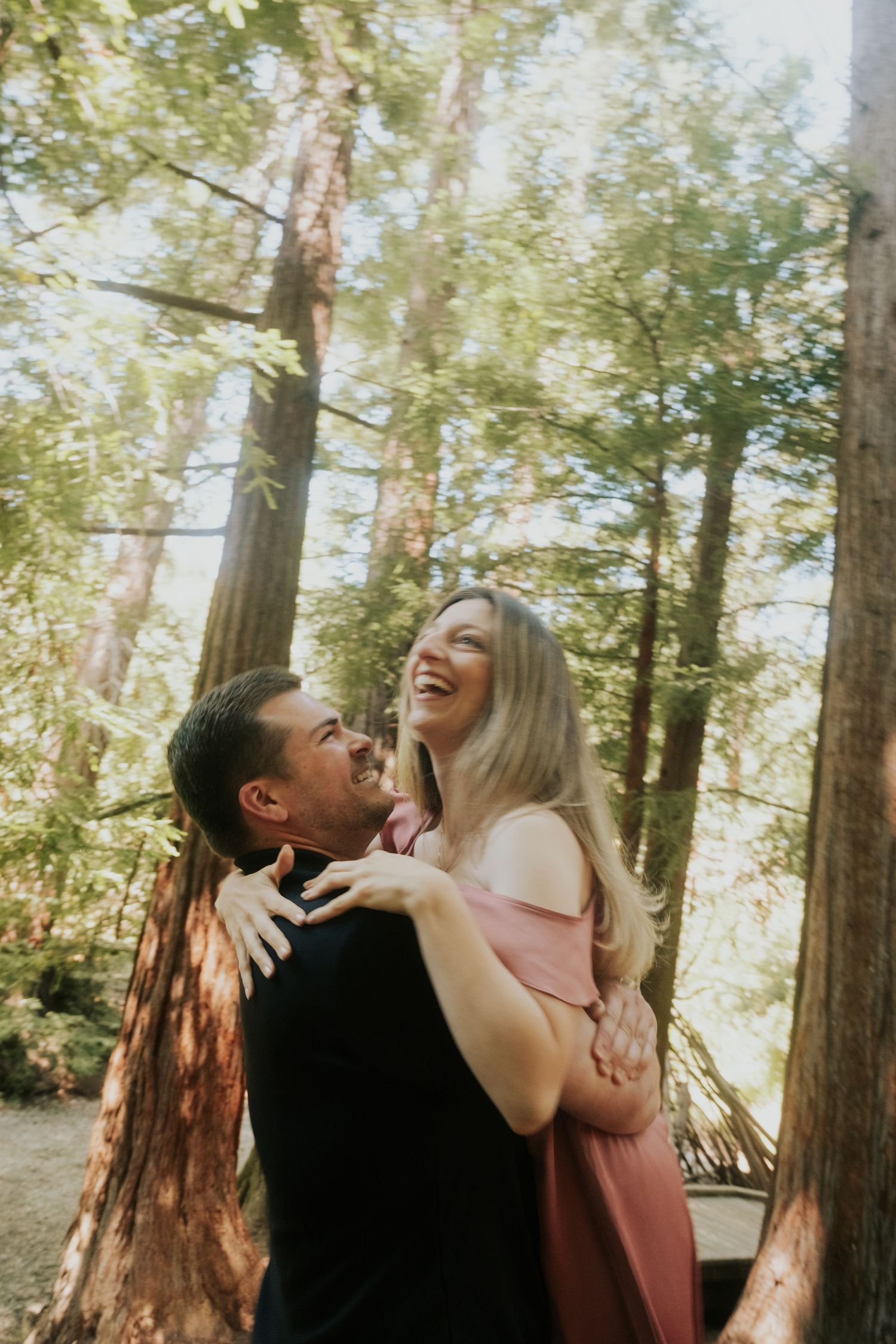 Joyful couple laughing together on nature trail surrounded by majestic redwoods.