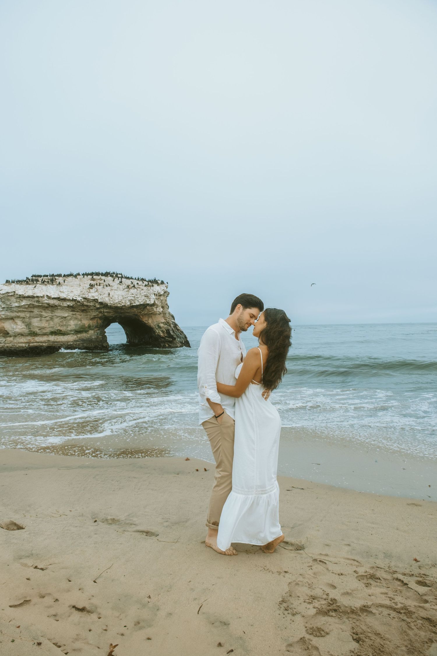 Romantic beach moment with natural stone arch and crashing waves in the background.
