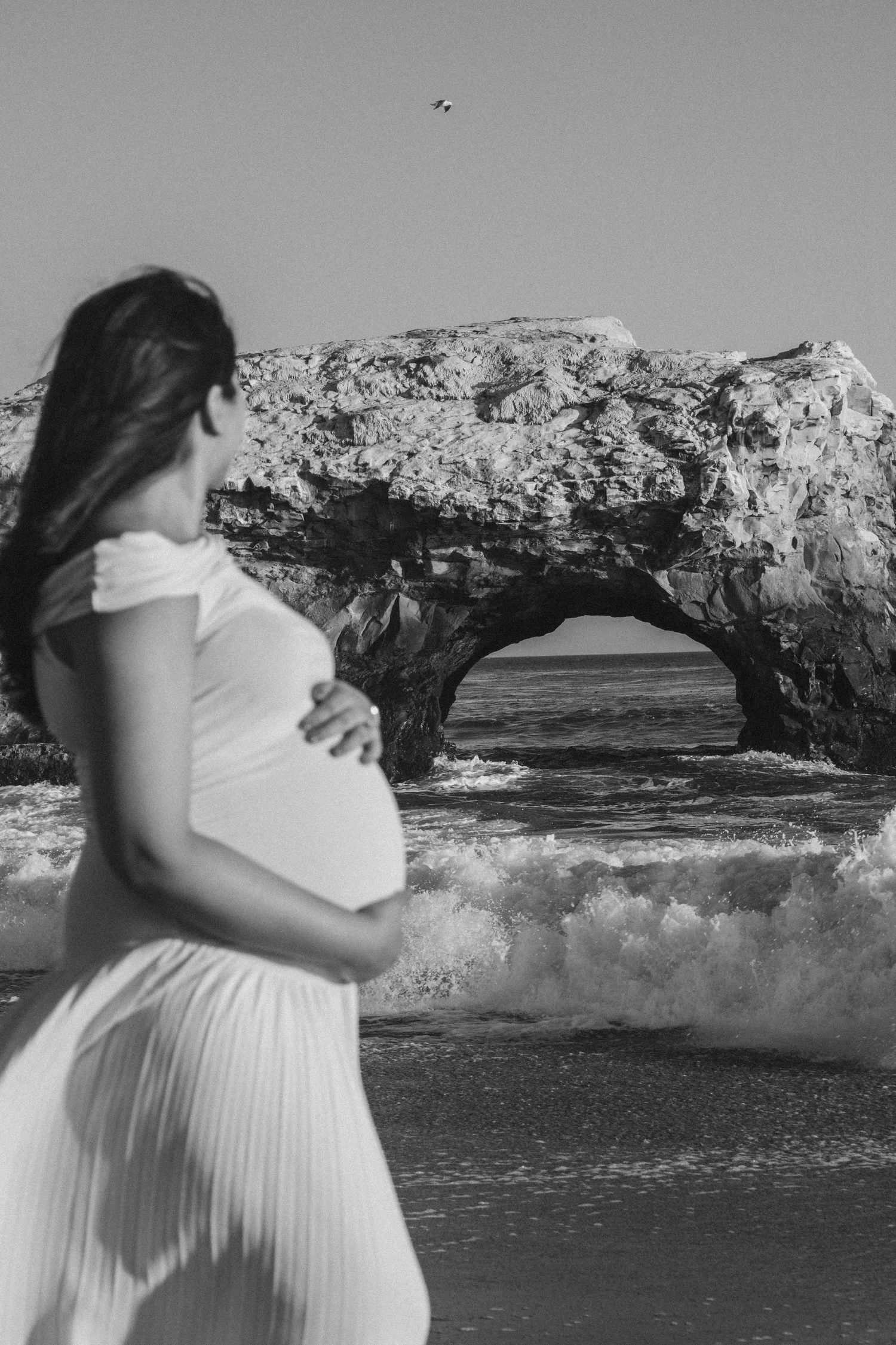 Maternity photos in black and white featuring dramatic ocean waves and rocky coastline.