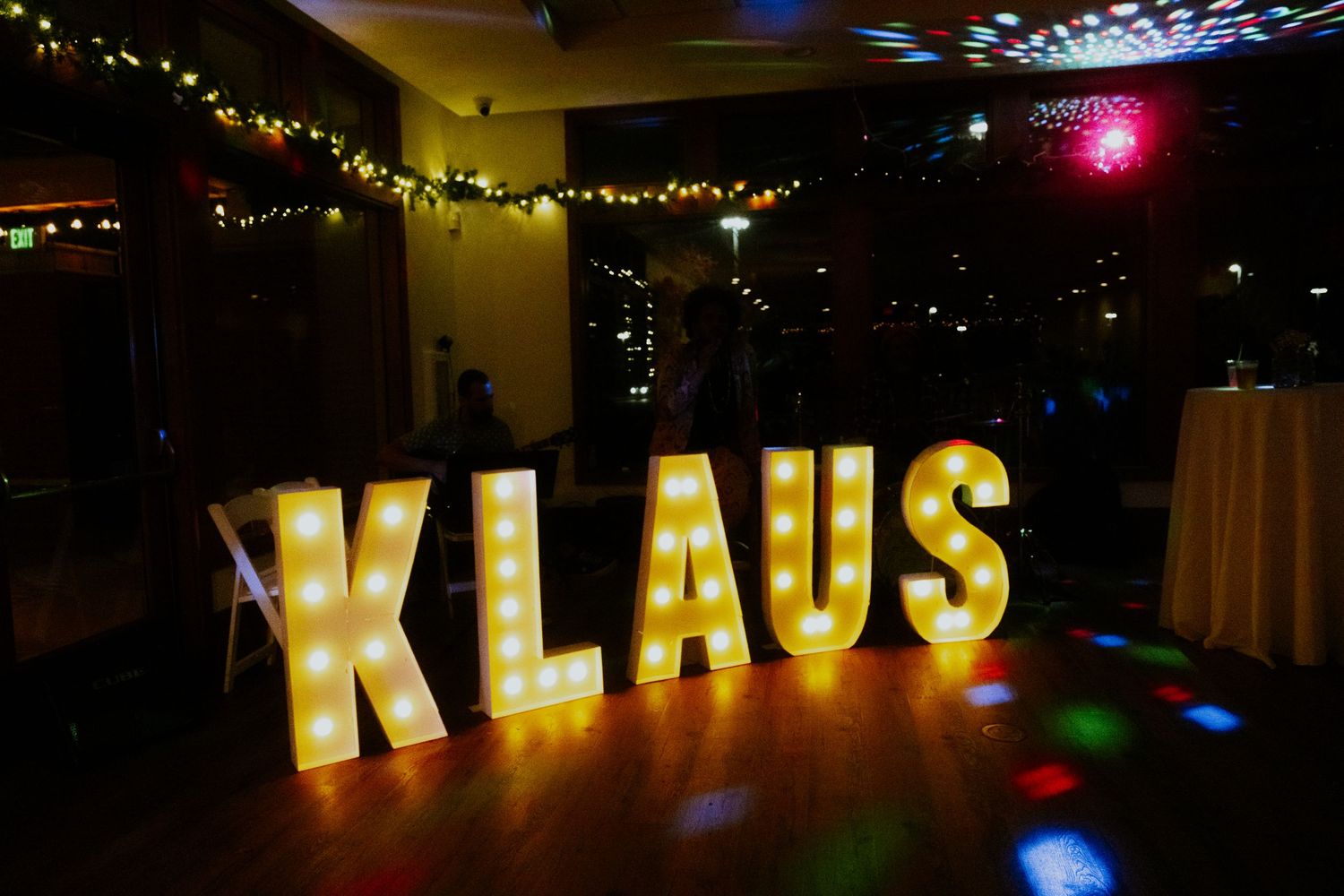 Large illuminated marquee letters spelling KLAUS on a dance floor with colorful disco lights and string lights.