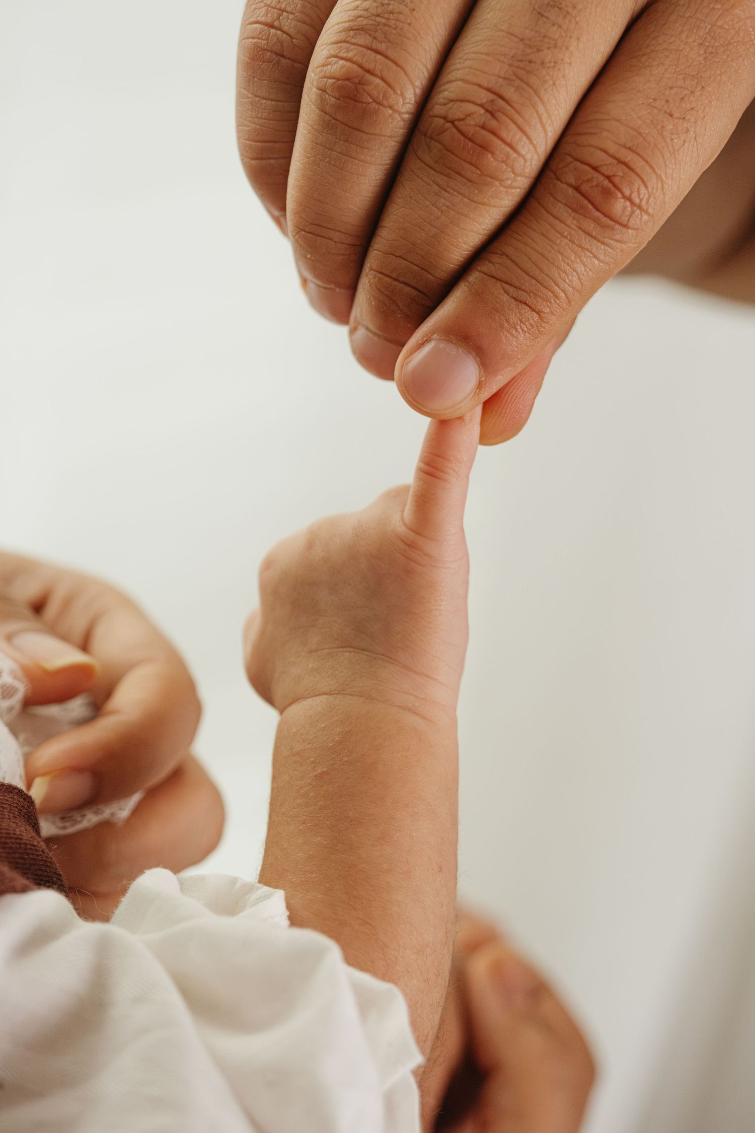 Gentle hands holding and touching tiny baby feet in white clothing.