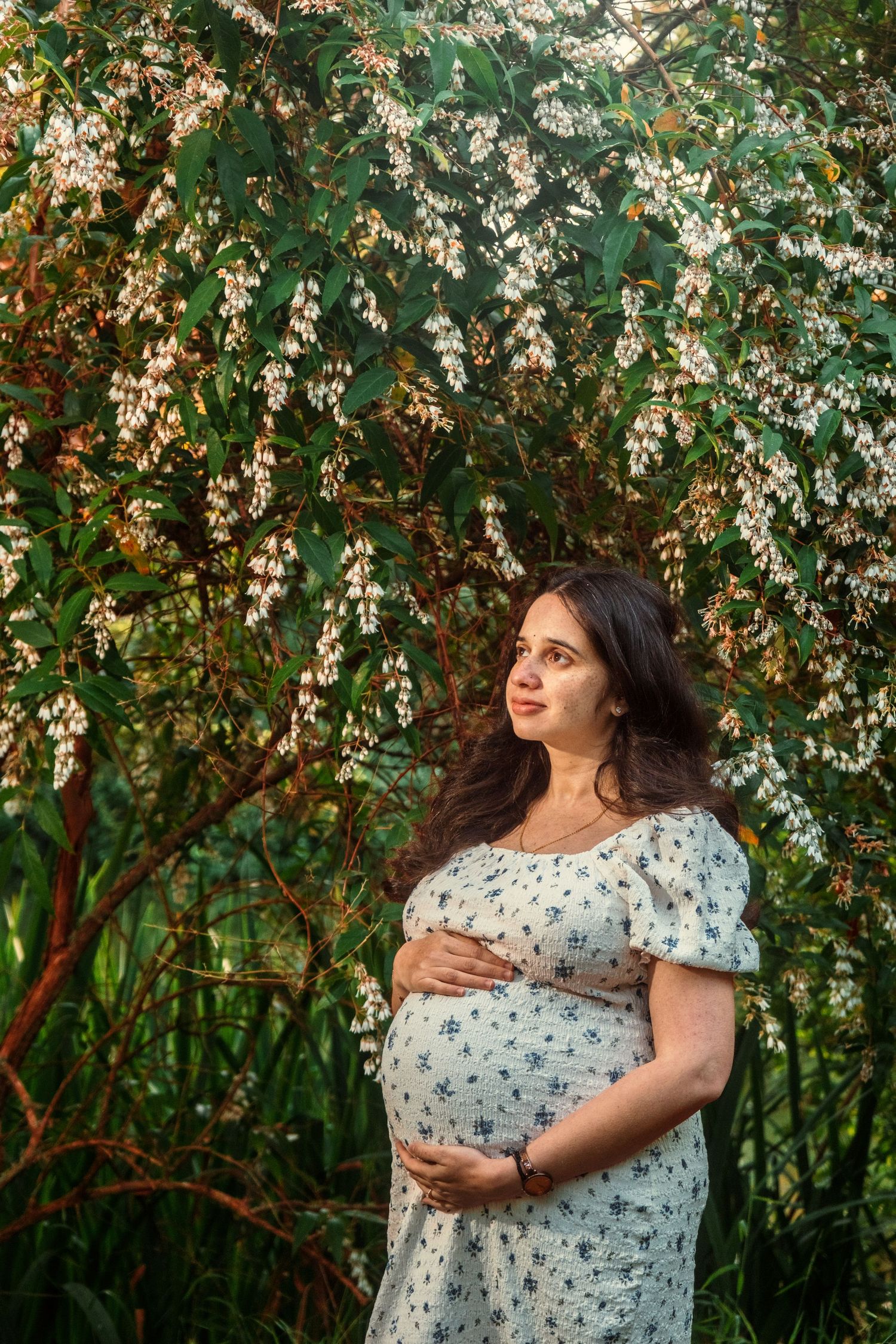 Woman in floral dress posing near blooming spring trees.