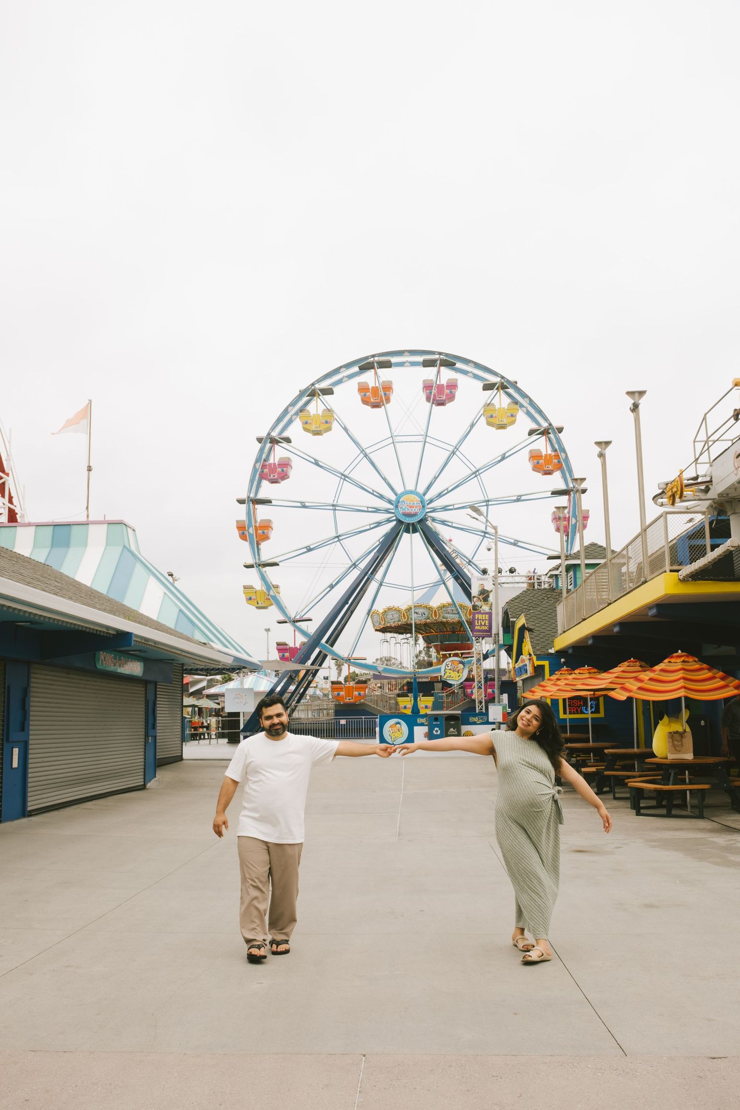 An empty boardwalk with colorful carnival rides and a Ferris wheel in the background.