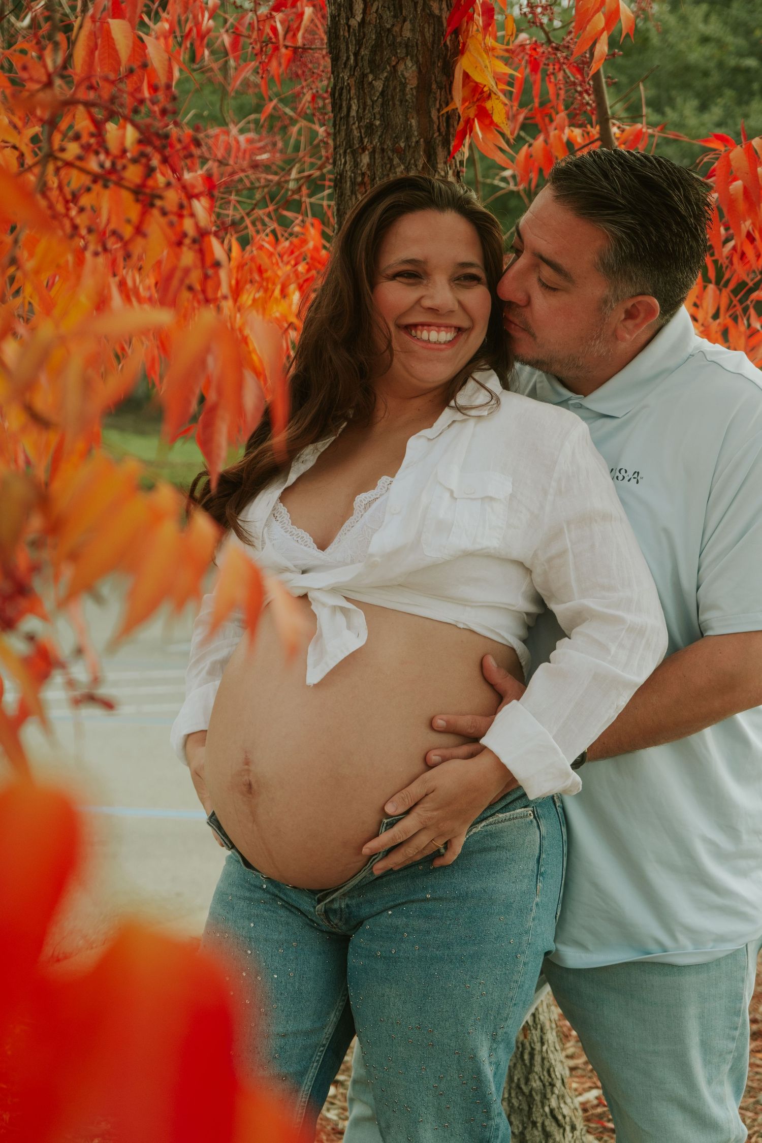 A couple shares an intimate moment among vibrant red autumn leaves.
