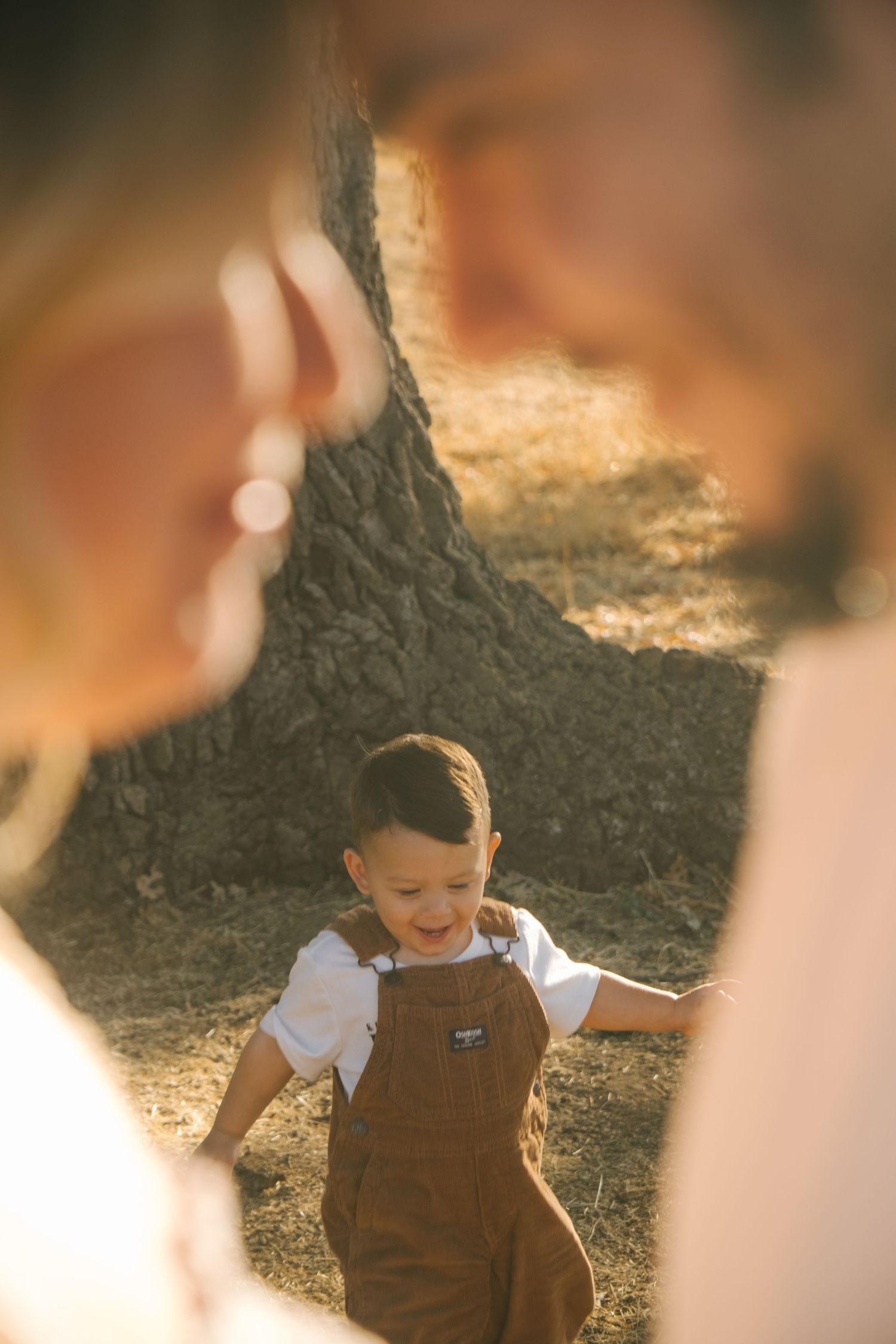 A toddler in brown overalls plays joyfully outdoors during golden hour.