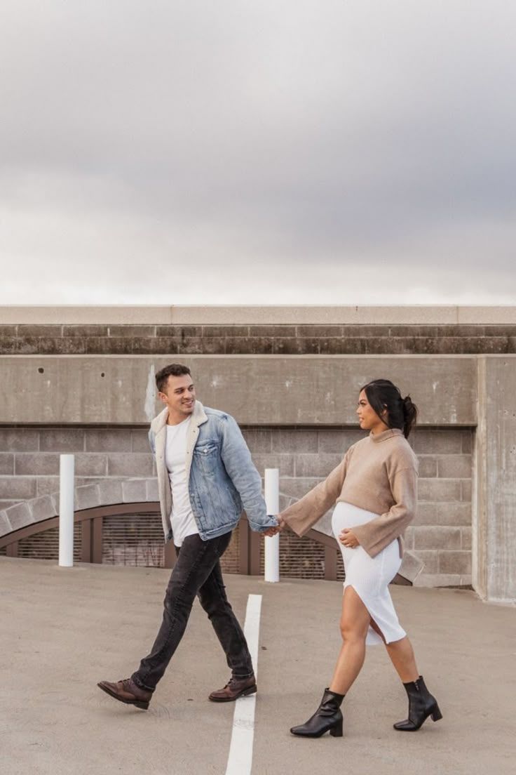 Playful couple dance moves photographed against concrete wall in outdoor setting.
