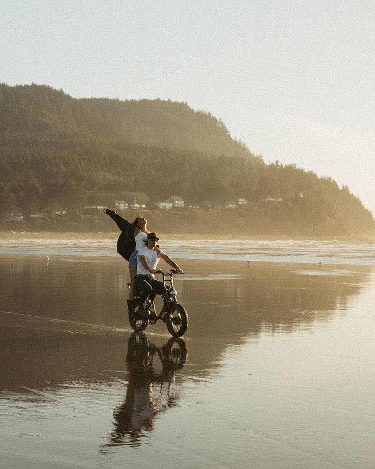 Silhouettes of people carrying bikes through shallow ocean water at golden hour.