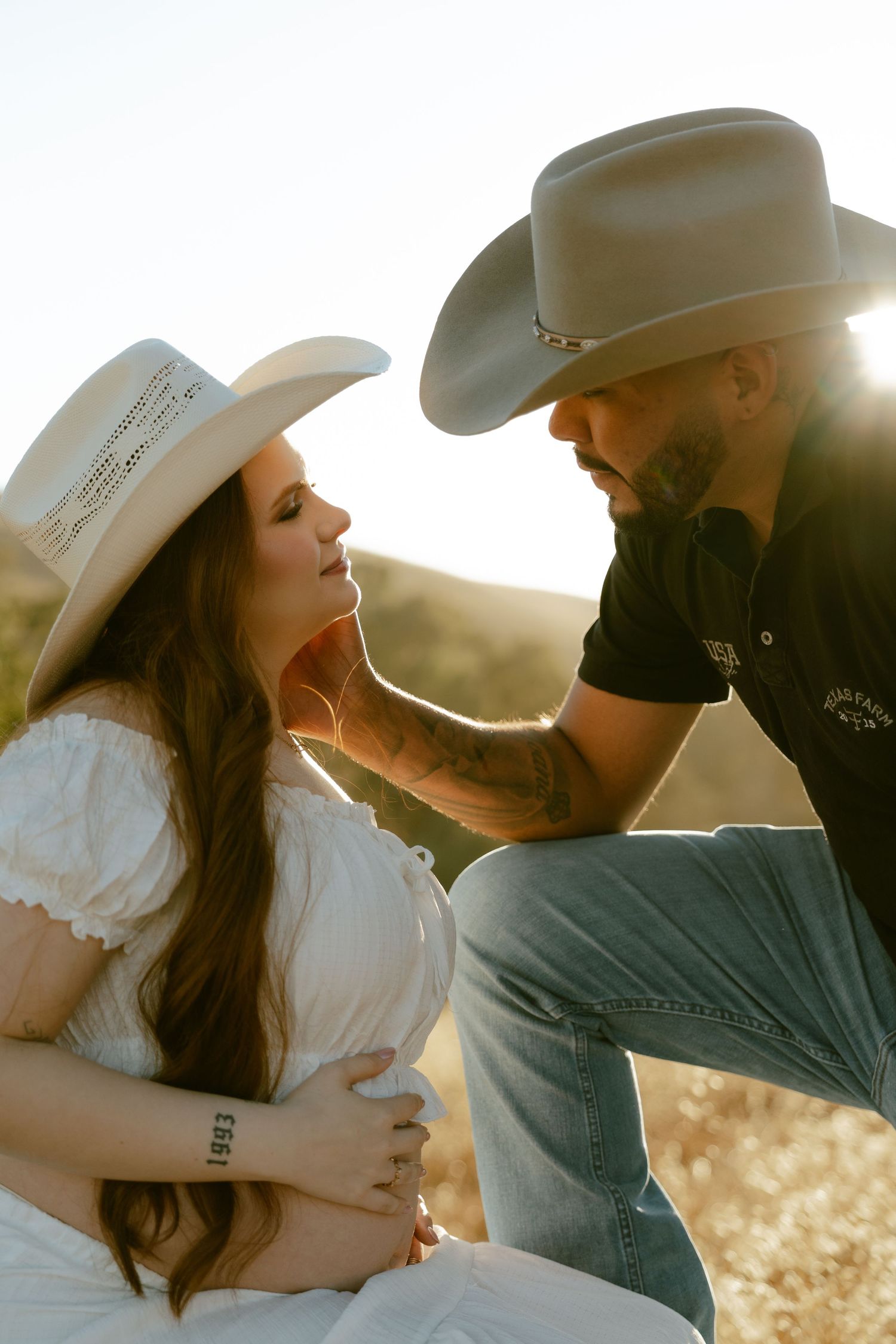 Couple in cowboy hats sharing a tender moment outdoors, man gently touching womans face in golden sunset light.