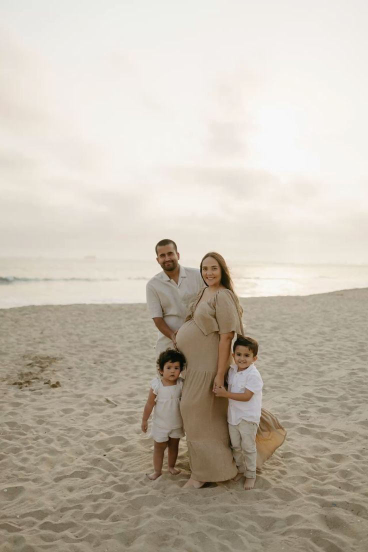 Family in neutral tones poses together on sandy beach during sunset photoshoot.
