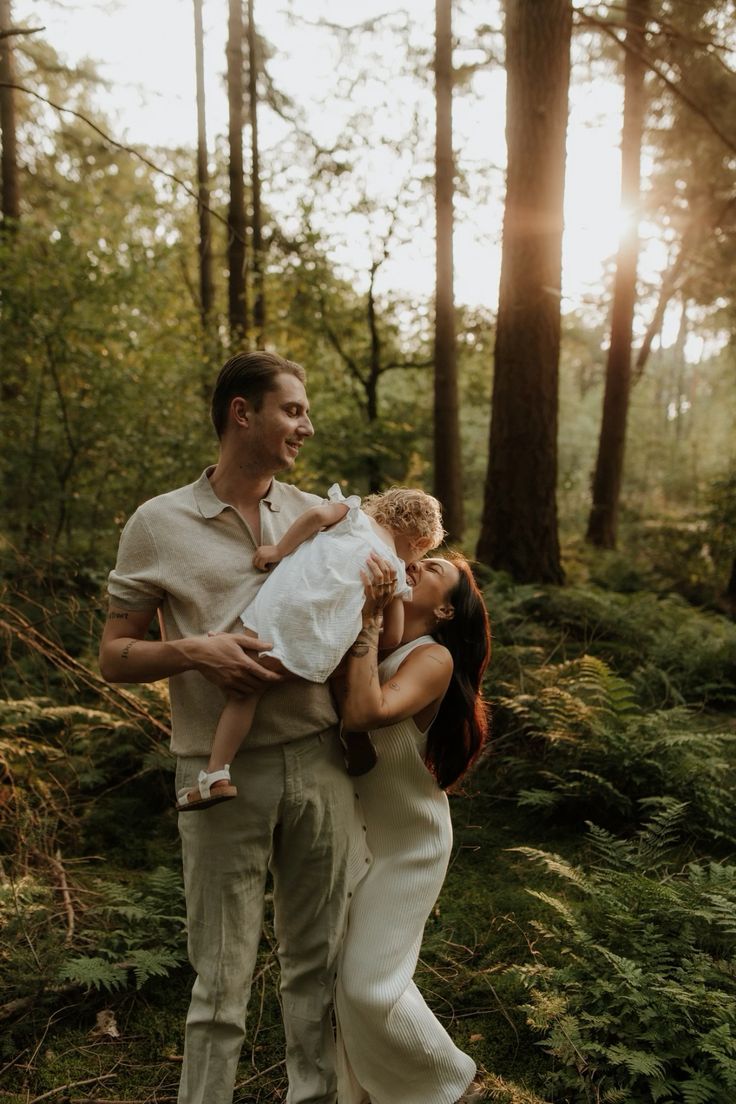 Couple shares tender moment in sunlit forest with ferns and tall trees.