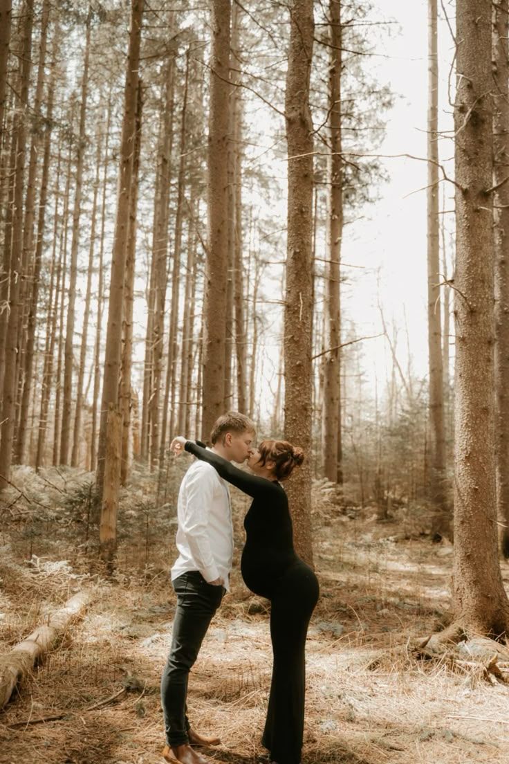 Couple shares intimate moment in sunlit pine forest.