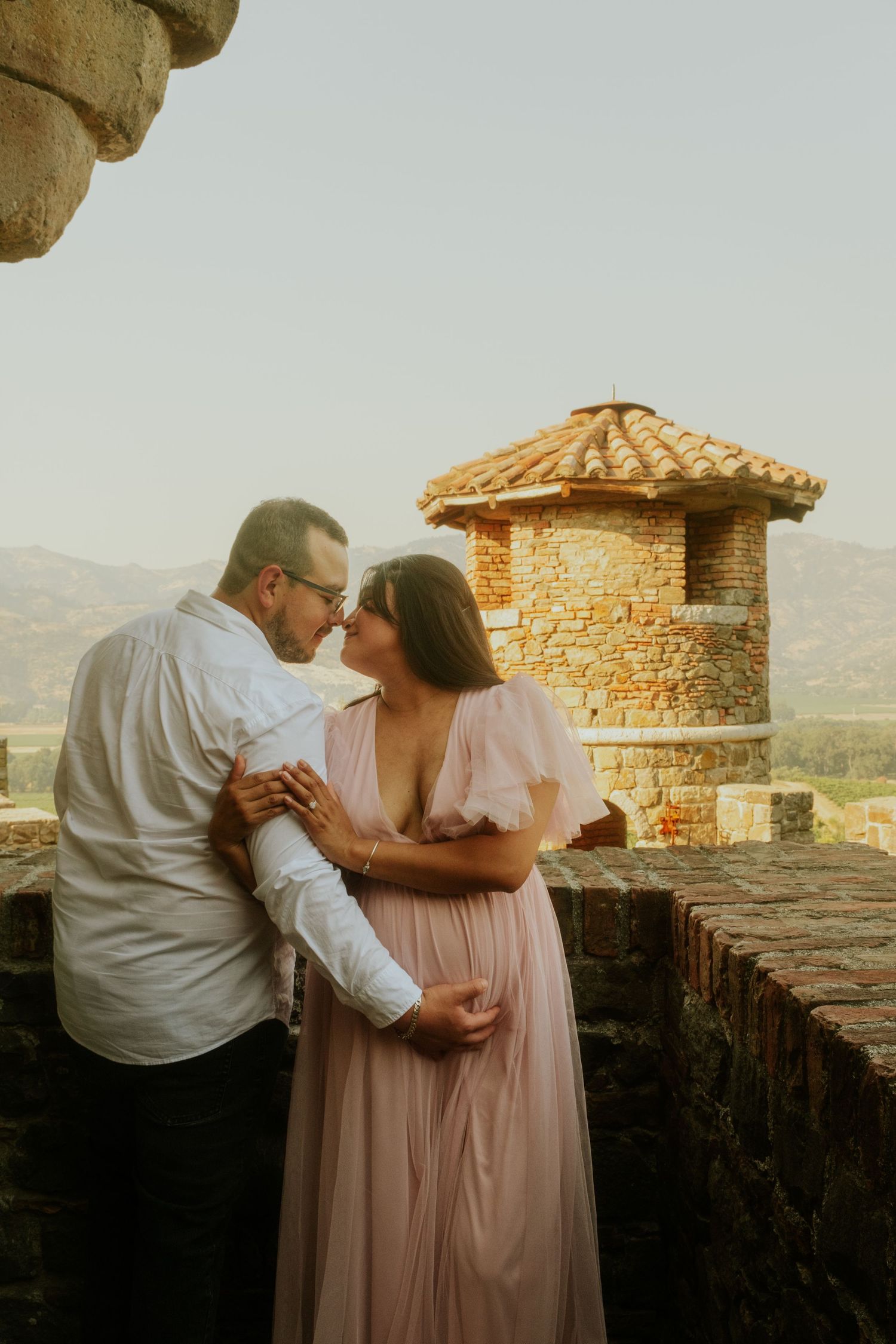 A couple shares an intimate moment on a castle terrace at sunset.