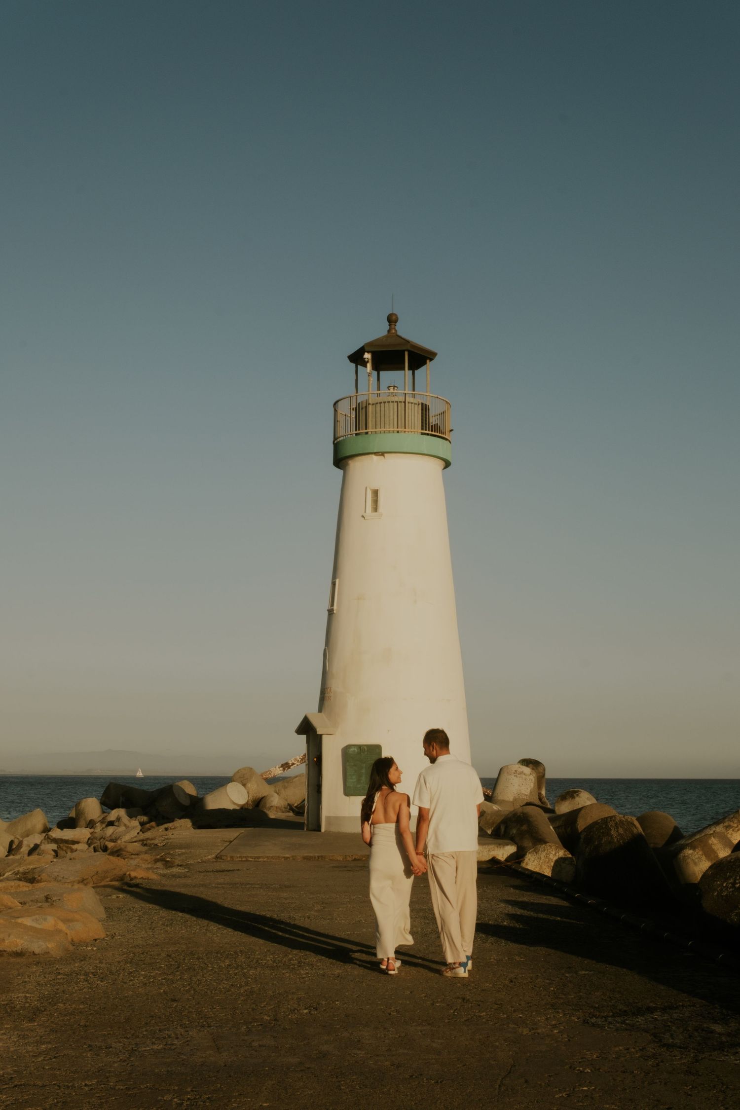 White lighthouse stands tall against clear sky with rocky shoreline.