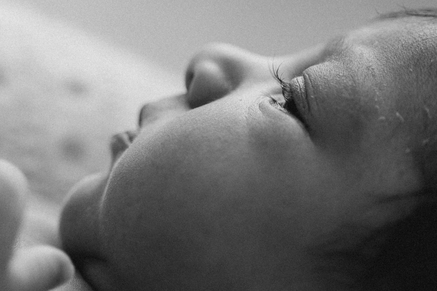 Close-up black and white photo of a newborn baby's face with wet skin, looking upward peacefully.