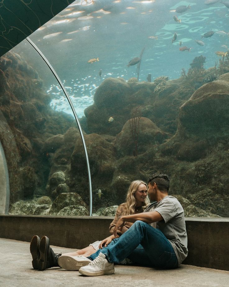 Romantic moment at an aquarium as couple lies on floor watching fish swim overhead.