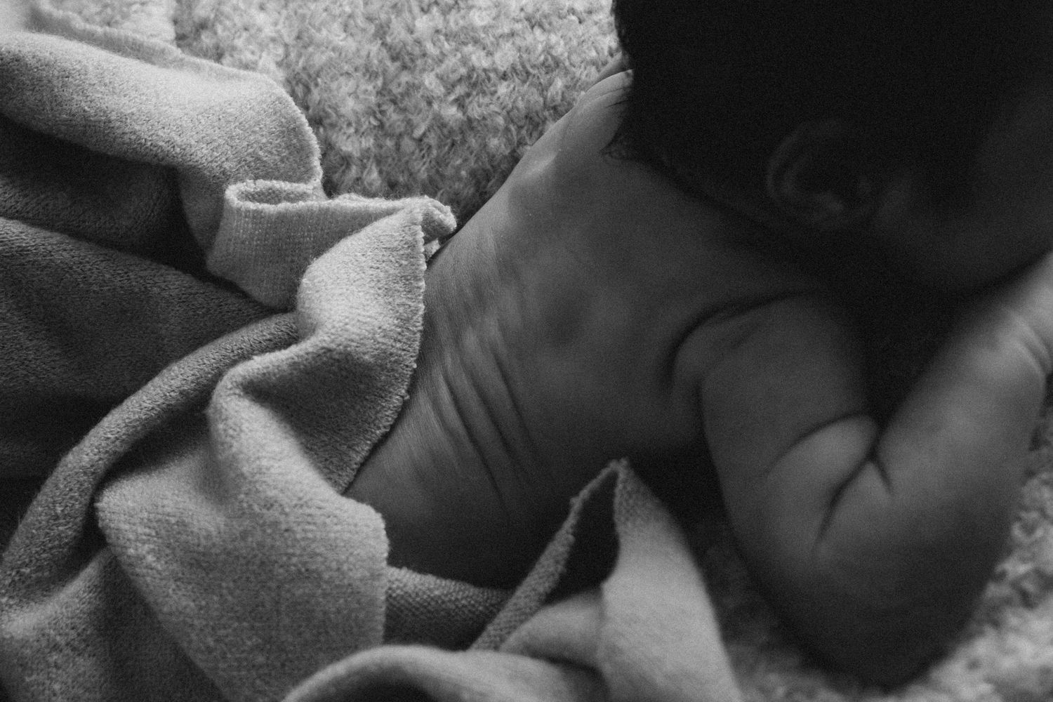 Black and white intimate portrait of sleeping newborn wrapped in soft blanket.
