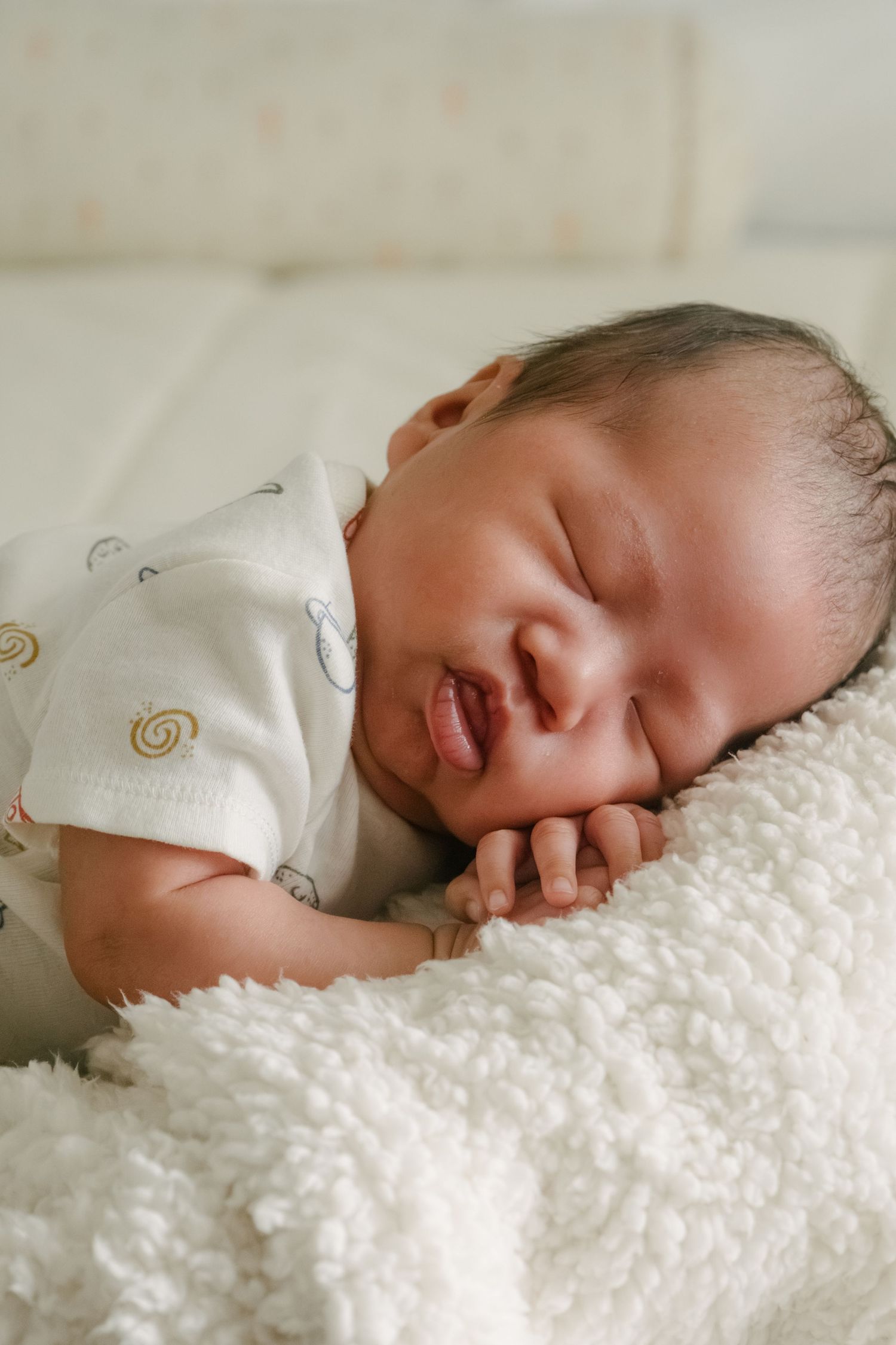 Baby napping on white textured blanket in soft natural light.