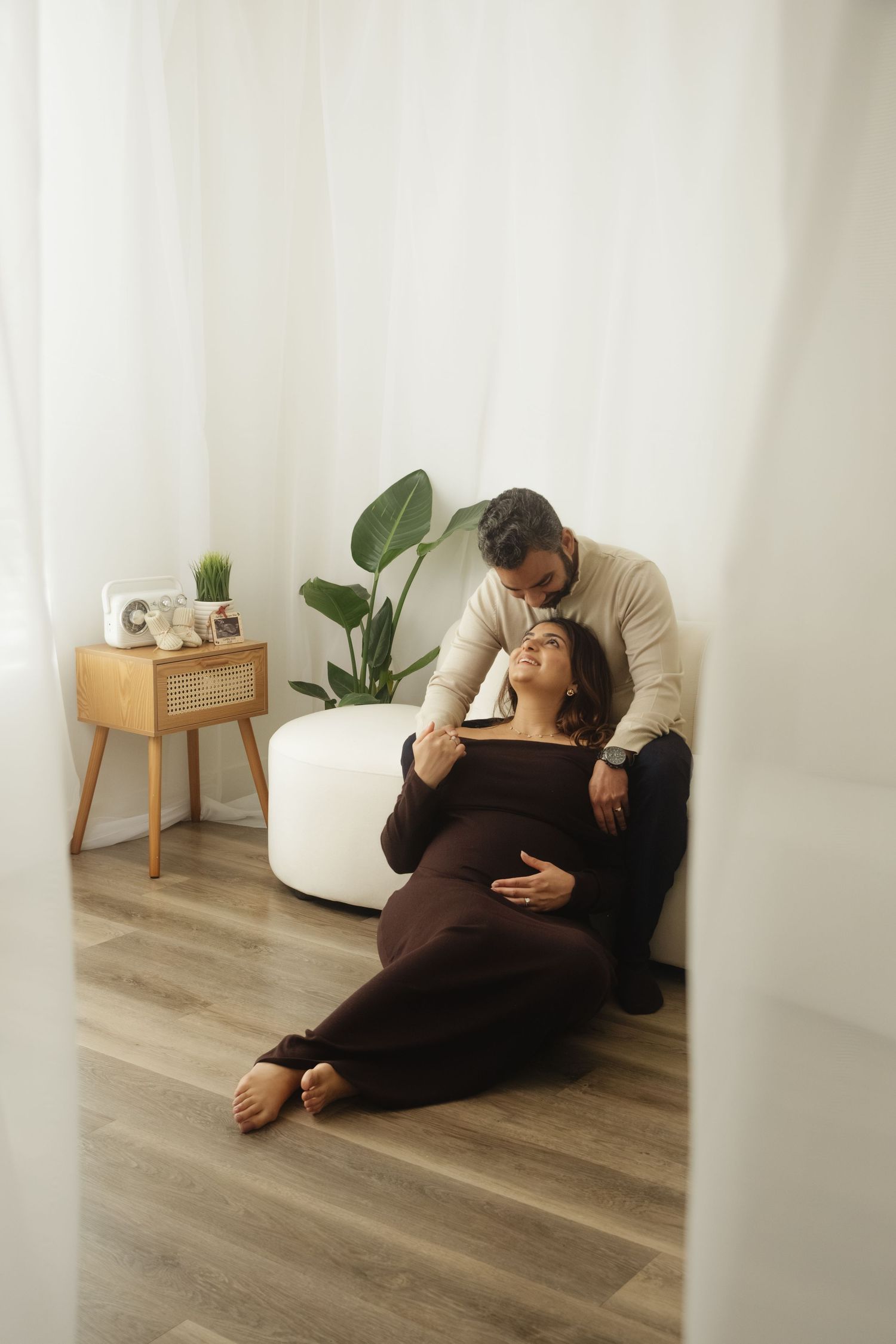 A couple shares a tender moment on the floor beside houseplants.