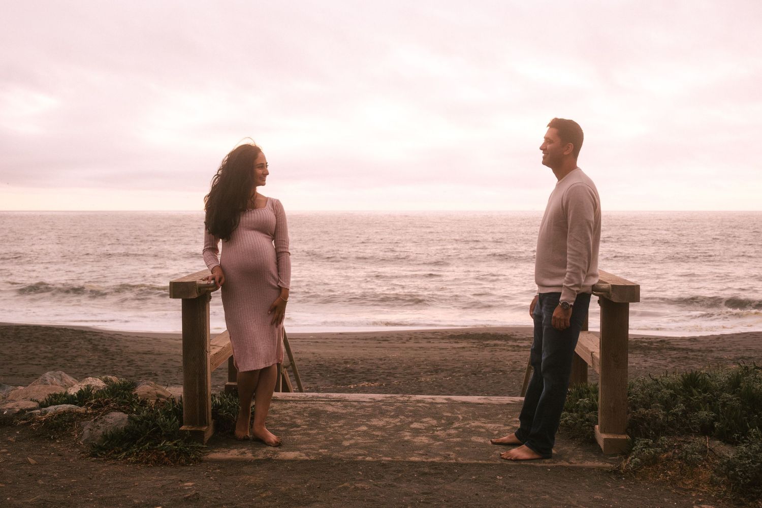 Couple sitting together on beach during sunset in romantic seaside photoshoot.