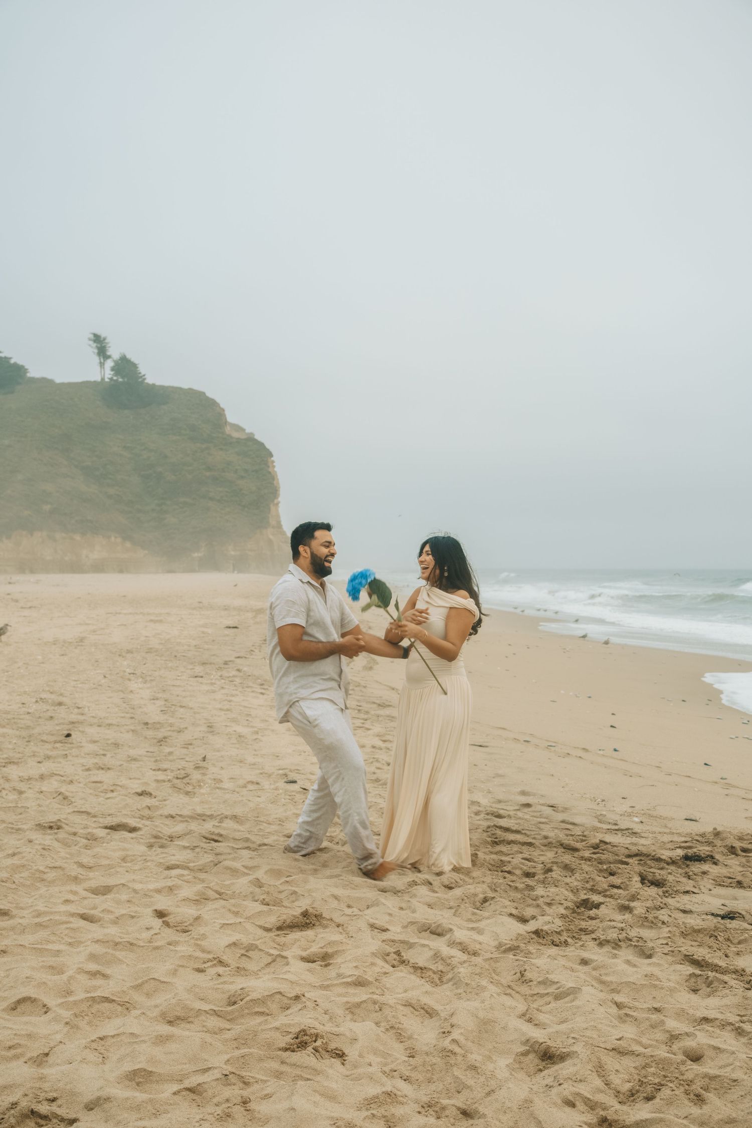 Couple plays with blue ball on sandy beach near coastal cliffs.