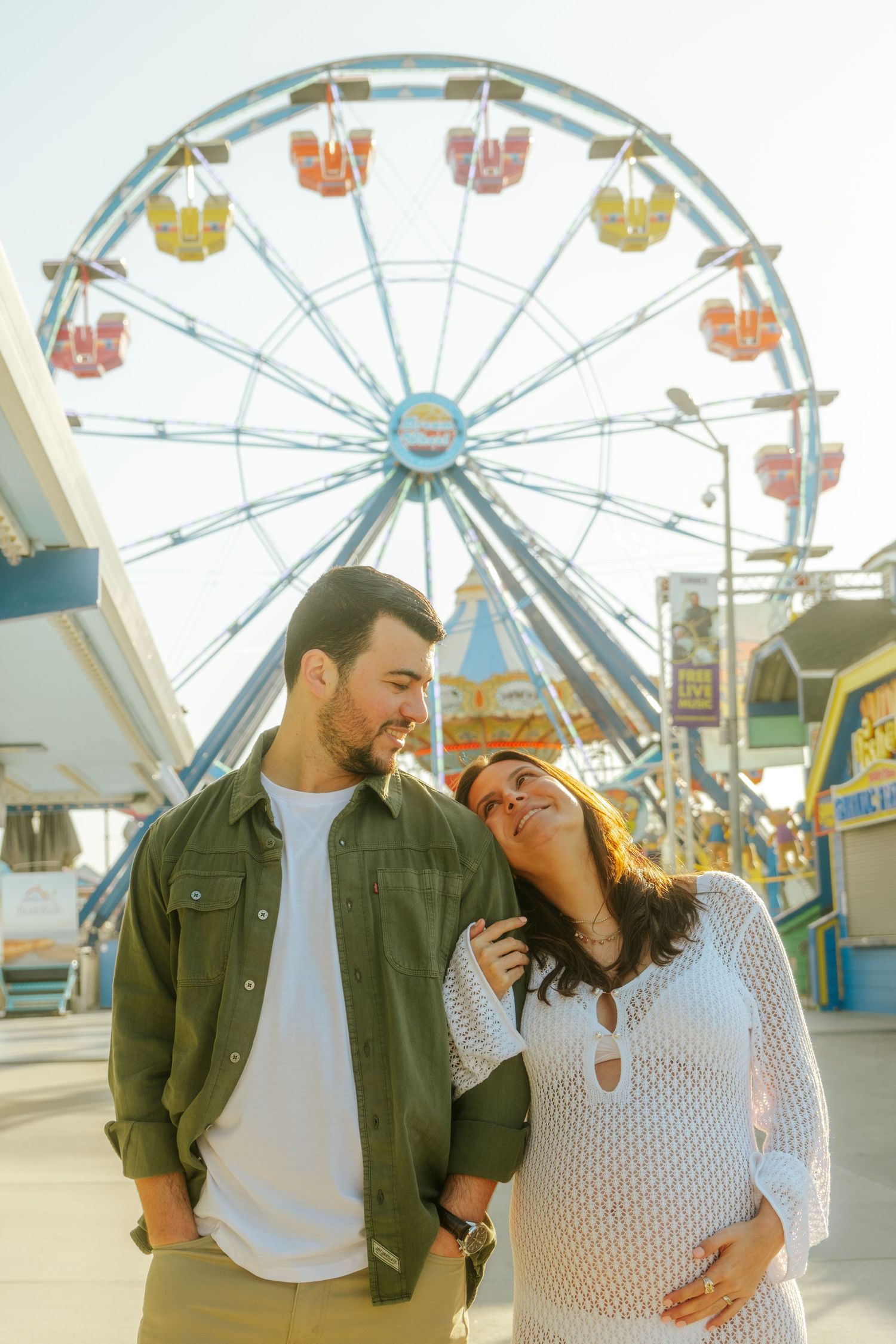 A couple shares playful moments in front of a colorful Ferris wheel at an amusement park.