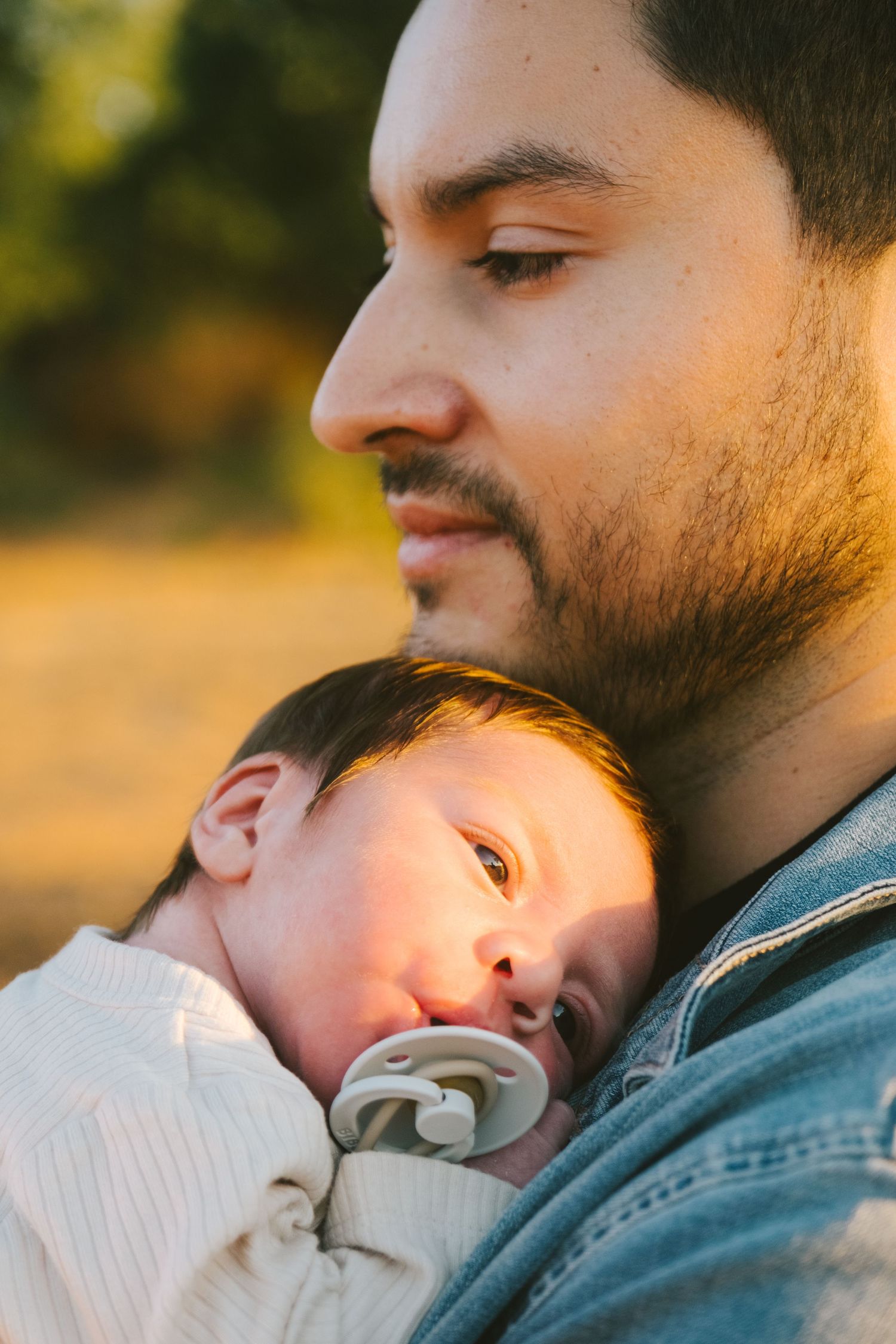 Intimate moment between parent and sleeping baby in warm evening sunlight.