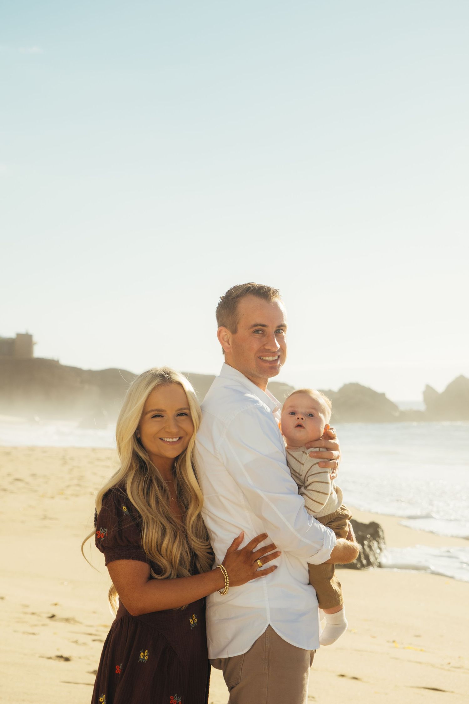 Family portrait on sunny beach with golden light and ocean backdrop.