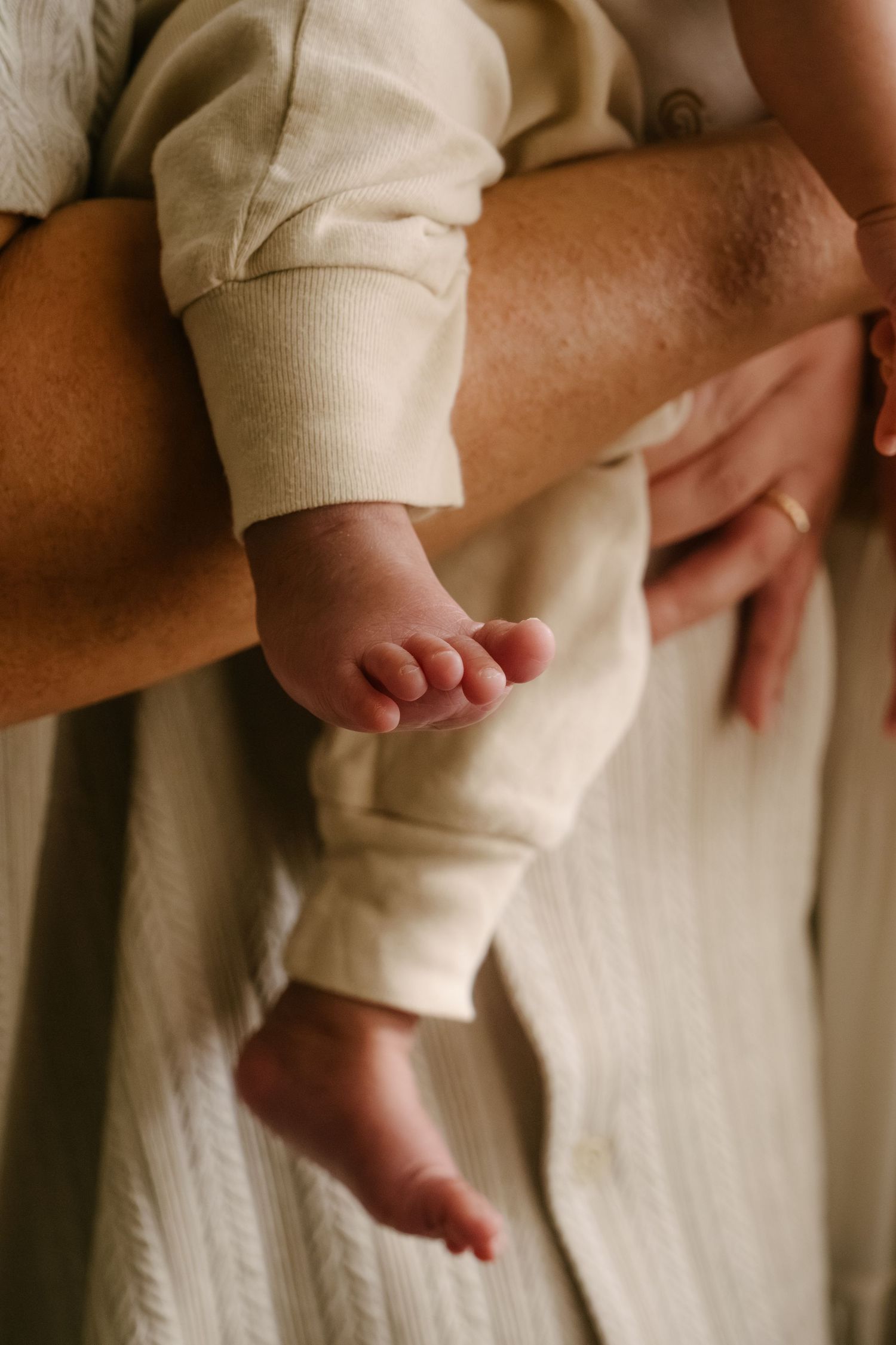 Baby's small feet being held by adult hands against white fabric.