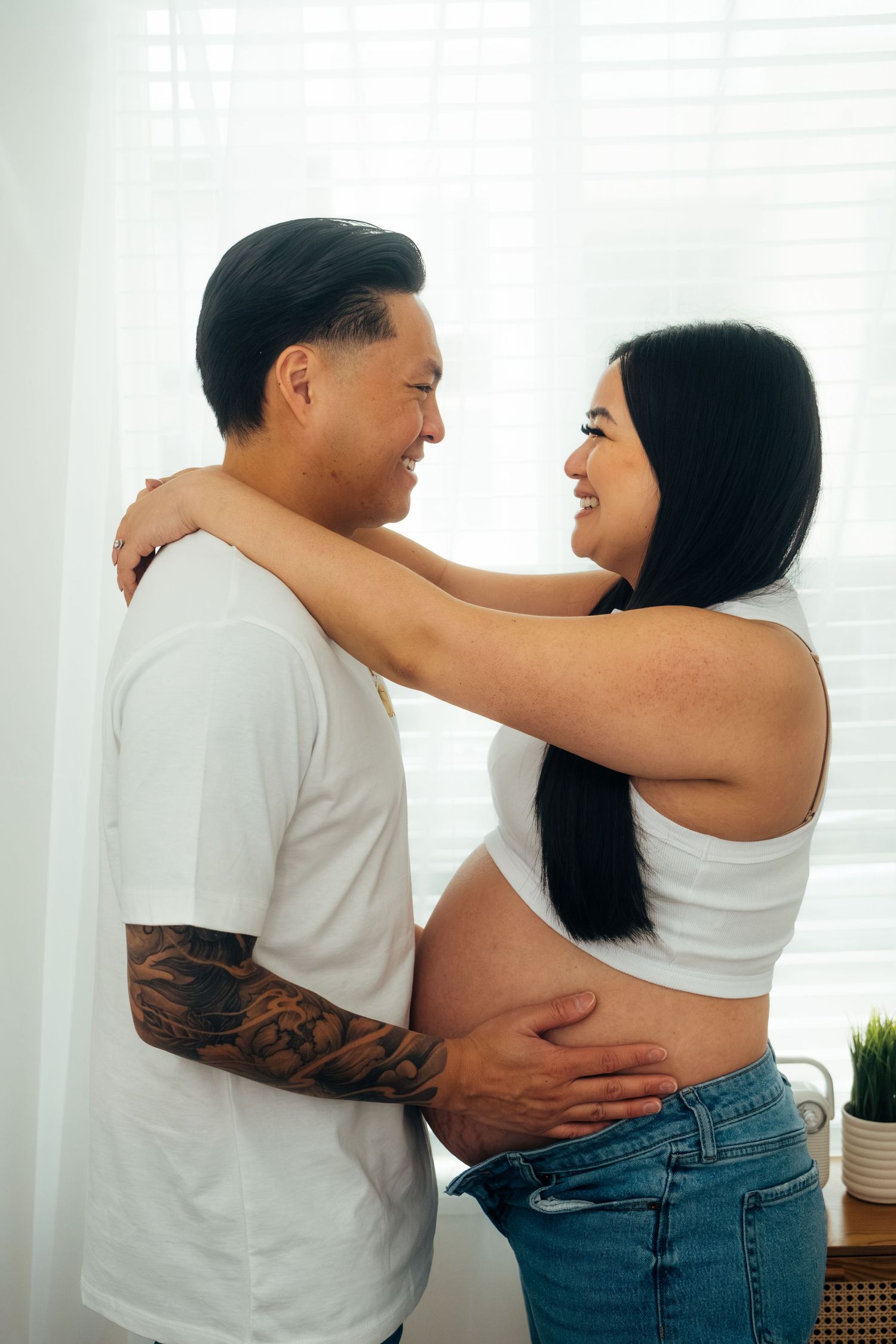 Couple in casual attire embracing in bright room with window.